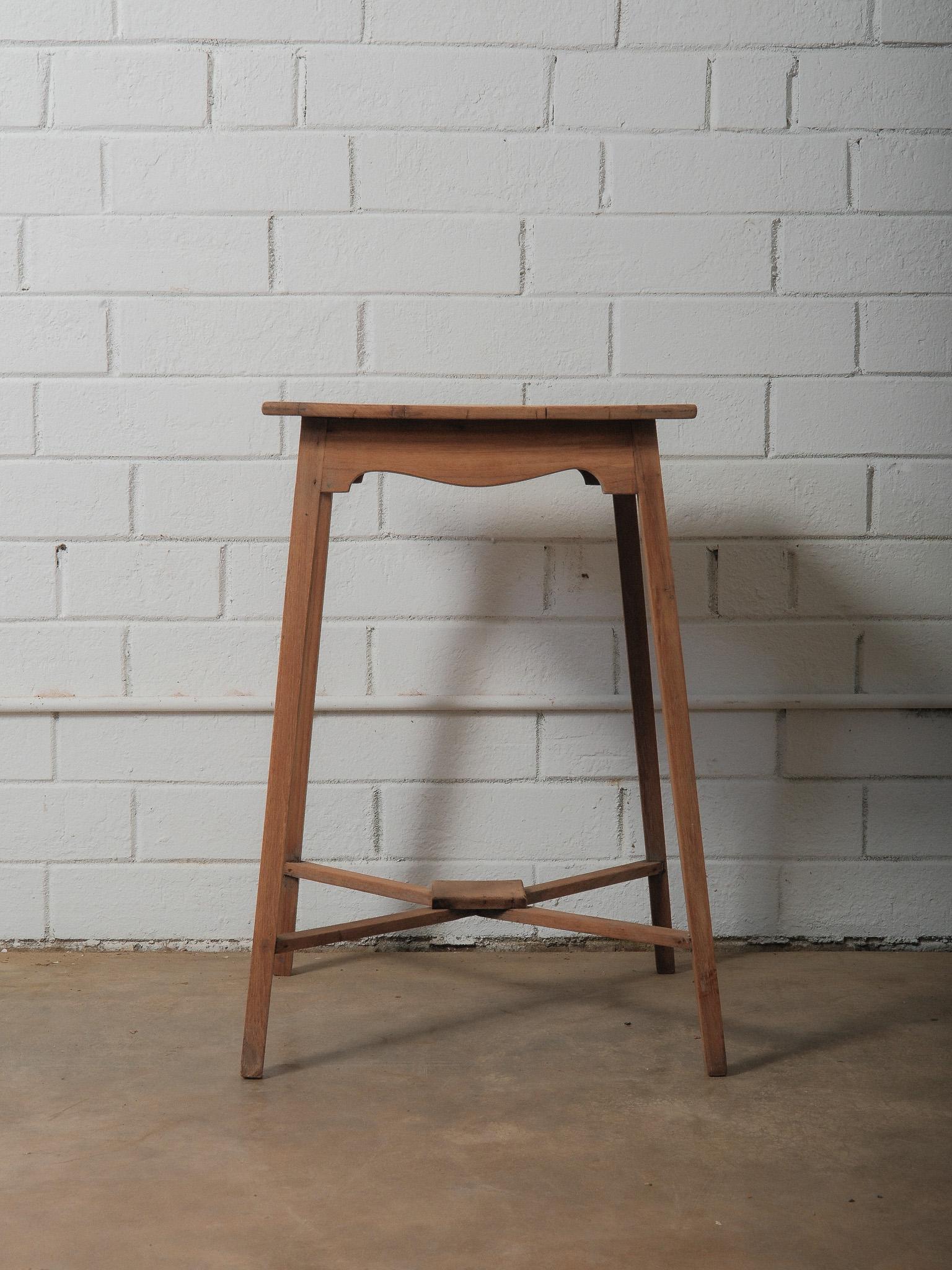 A small wooden table defined by its slender proportions and straightforward construction. The rectangular top is formed from three joined planks, each showing natural grain patterns and light surface wear. Below, the apron is cut with a subtle