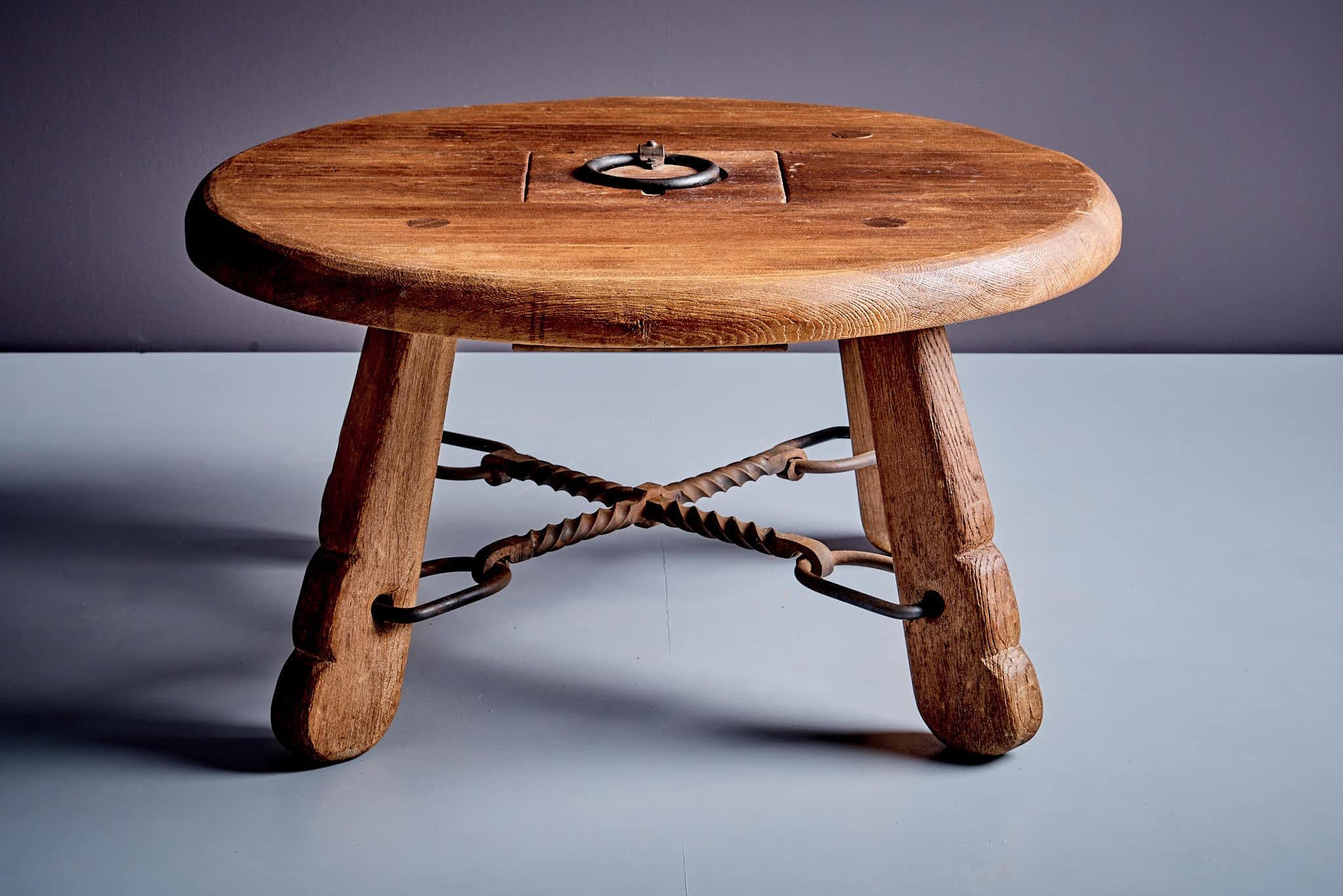 Rustic solid oak table with wrought iron details. Features a round top, carved legs, and a hidden storage compartment. Compact and sturdy, perfect for vintage or rustic decor. Its compact, round design features a sturdy wooden top, carved legs, and