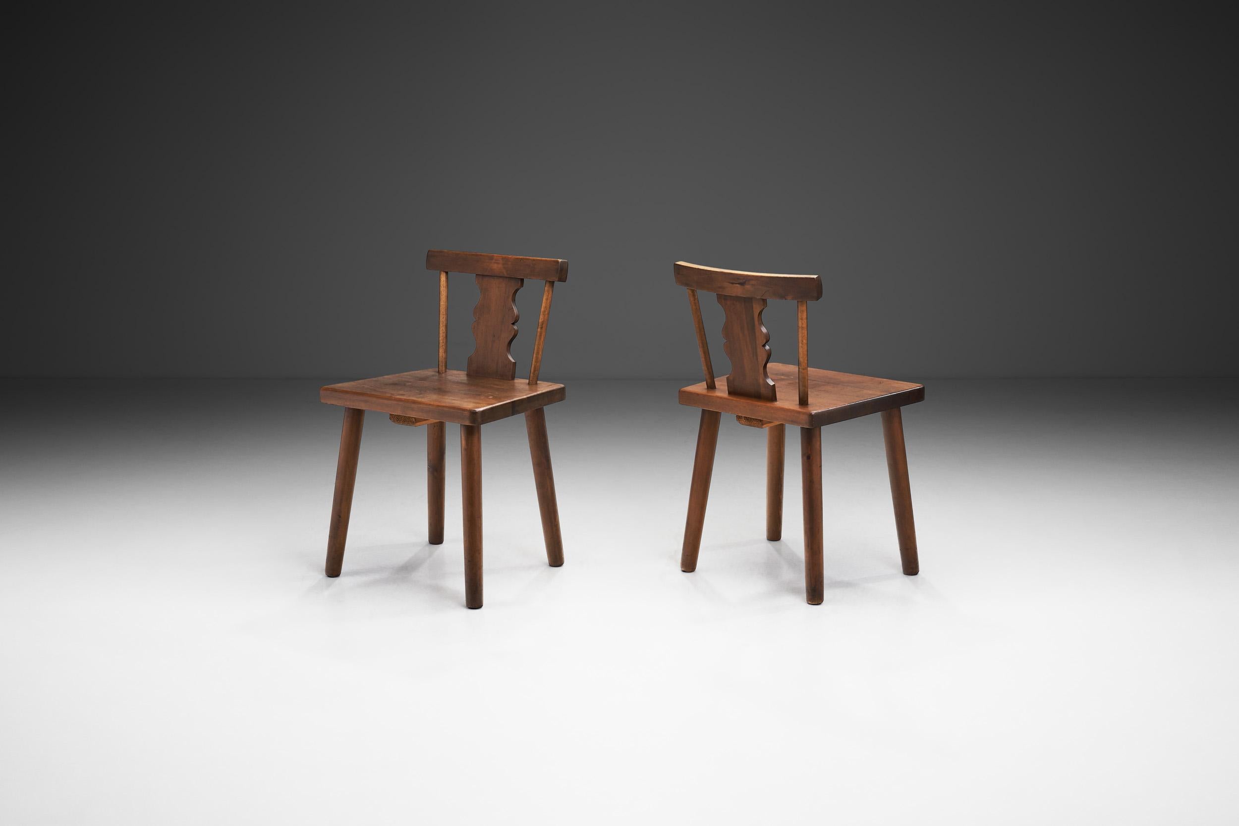 This one-of-a-kind pair stands as evidence to the enduring charm of handcrafted furniture. These chairs tell a story of craftsmanship, history, and the timeless appeal of rustic beauty. These chairs, with their weathered pine and hand-carved backs,