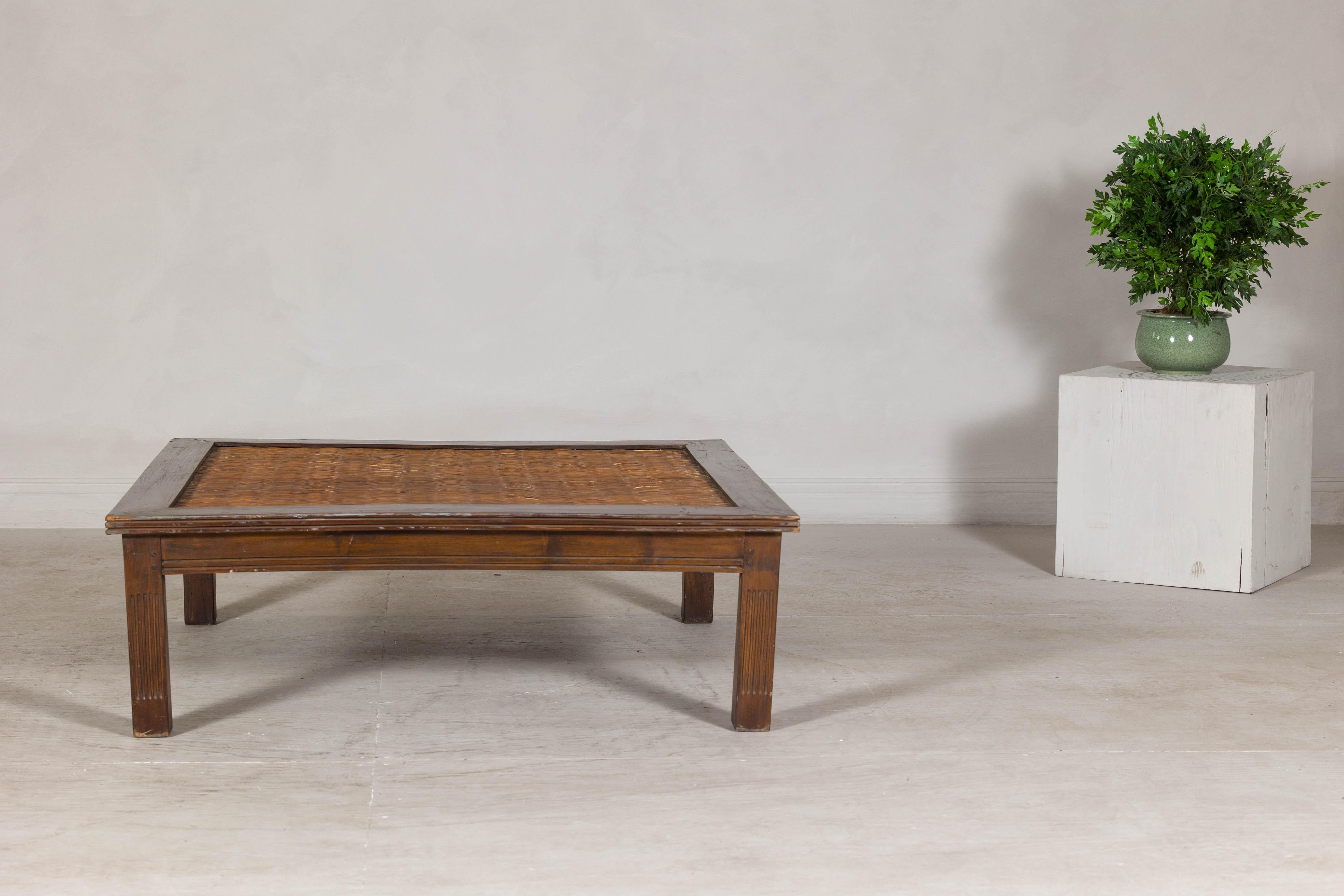 This vintage low table features a richly patinated wood frame surrounding a handwoven rattan inset, offering a distinctive blend of natural materials and clean-lined construction. With its square form and substantial proportions, it functions
