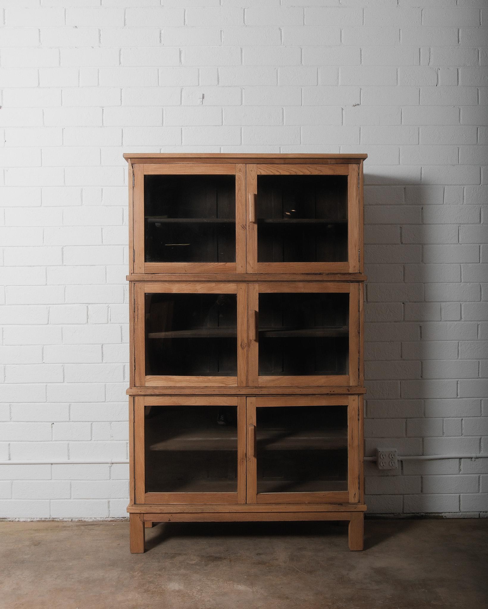 This is a rustic, multi-tiered glass-front display cabinet crafted from natural, unfinished wood, giving it a raw and organic aesthetic. The cabinet features three stacked sections, each with a pair of framed glass doors fitted with simple,