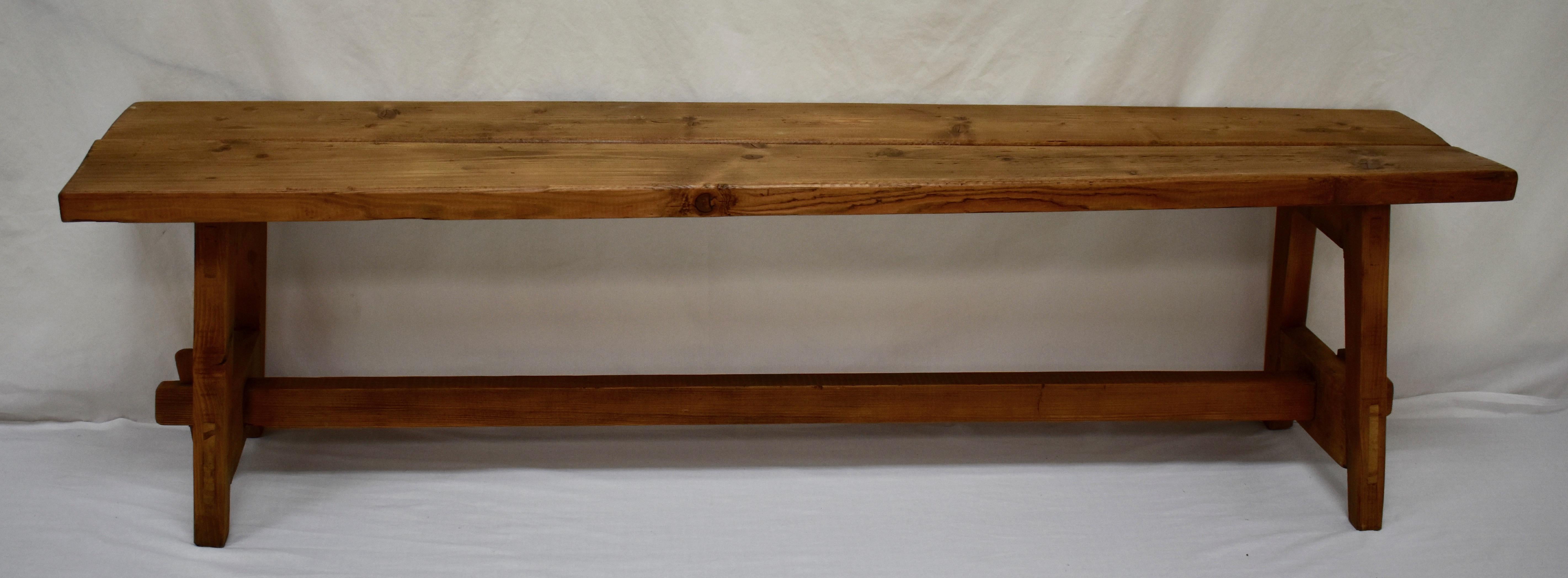 This is a rustic bench of great strength with an unusual form and a good deal of character. The members that form the splayed “A” frame trestle ends are through-tenoned for strength and stability, mortised into the underside of the top boards and