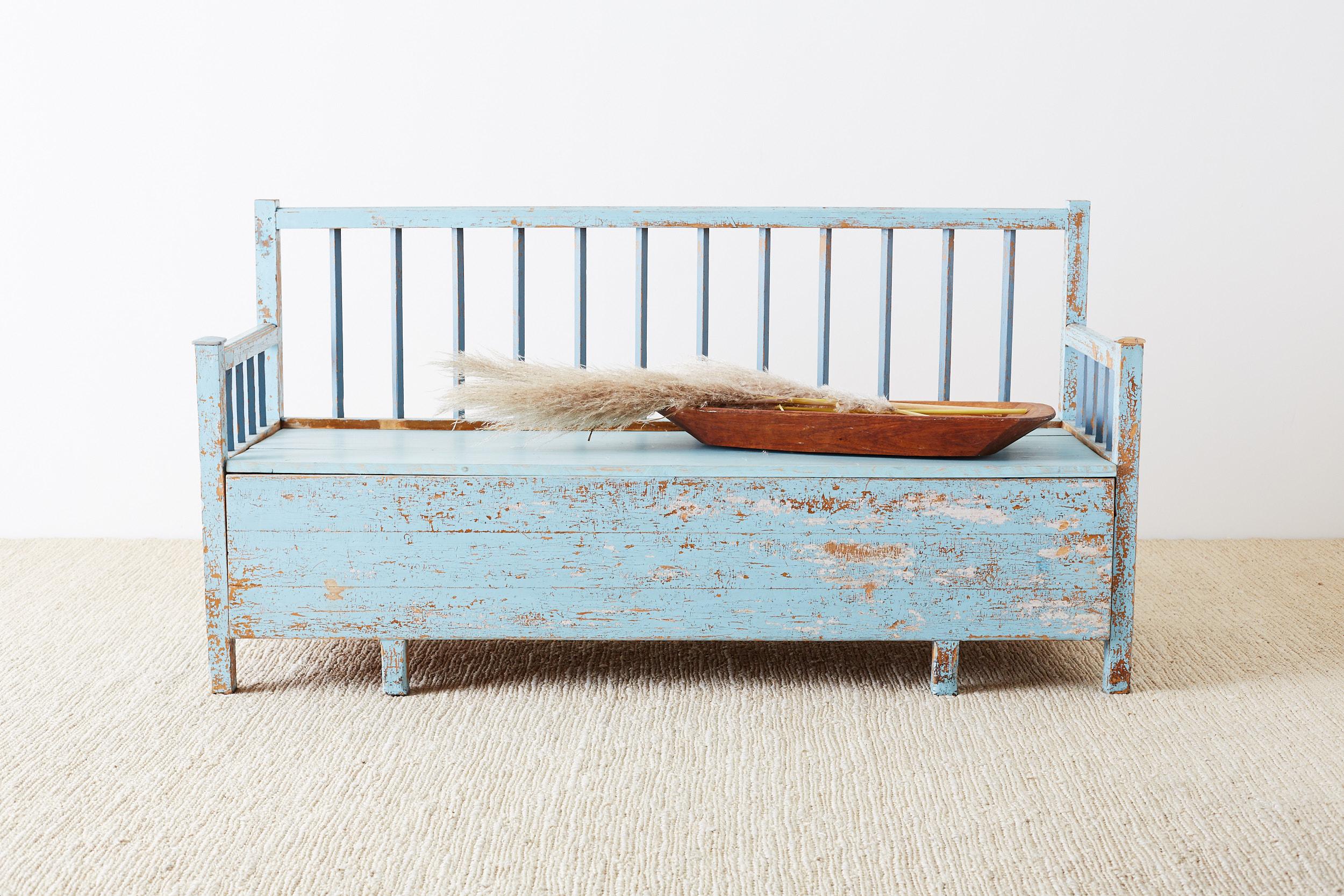 19th century rustic Swedish farmhouse storage bench or settle made of pine. Features a painted finish that is beautifully distressed and faded. The front of the bench seat slides out to reveal a 66 inch long by 21 inch wide storage area. The back