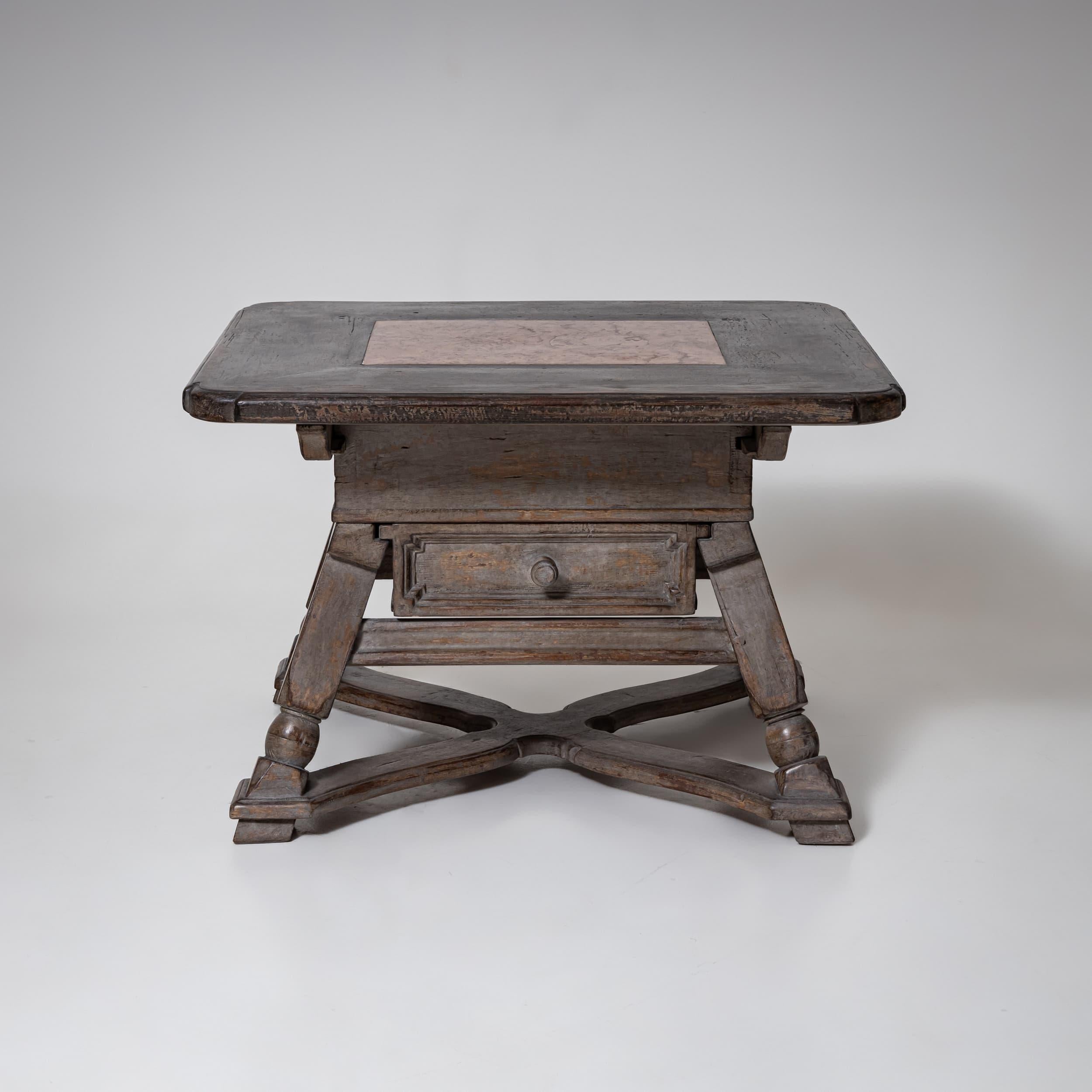 Table provinciale rustique, reconvertie en table basse. La construction en bois massif se caractérise par des pieds tournés et une base décorative en croix. Le plateau de la table est rehaussé d'un panneau de marbre encastré, ce qui ajoute une