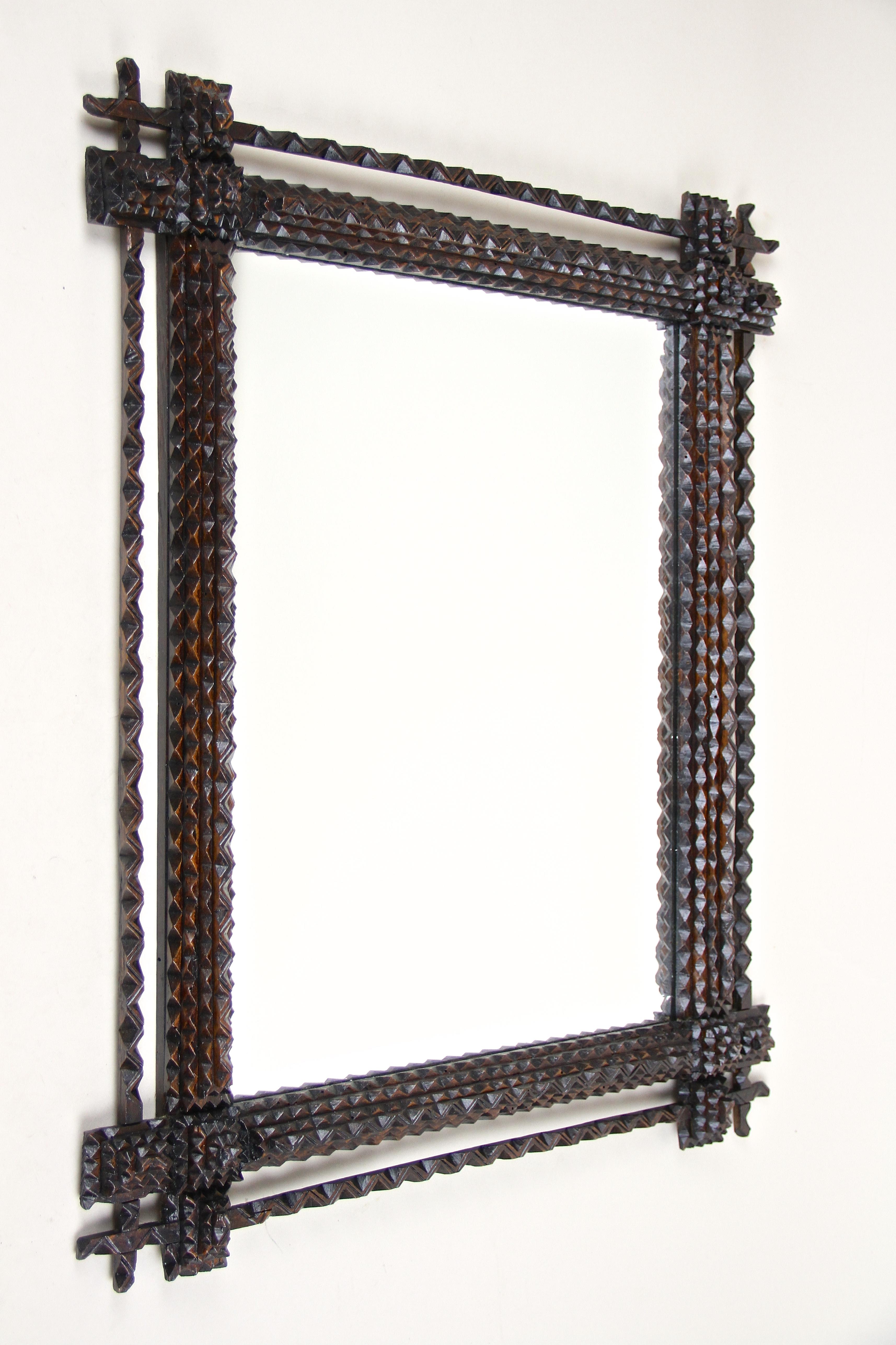 Unusual rustic Tramp Art mirror from the late 19th century in Austria around 1870. This wooden wall mirror has been effortfully hand carved out of basswood and comes with a dark brown stained surface in great original condition. Highlighted with a