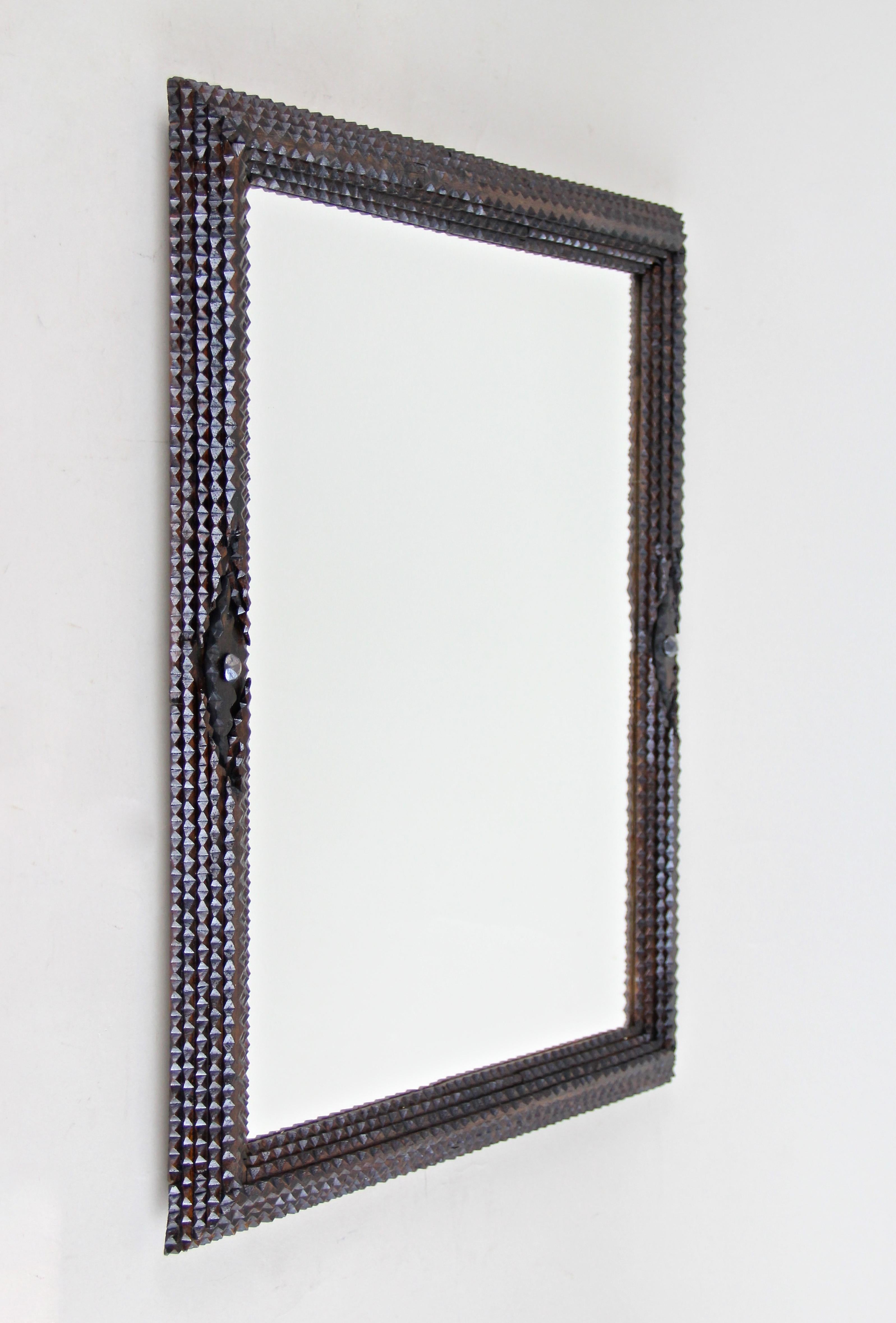 Charming rustic tramp art mirror from the late 19th century, circa 1880. This Austrian wooden wall mirror has been hand carved out of basswood and shows a light varnish sealed surface. The broad frame impresses with elaborate chip carvings and two