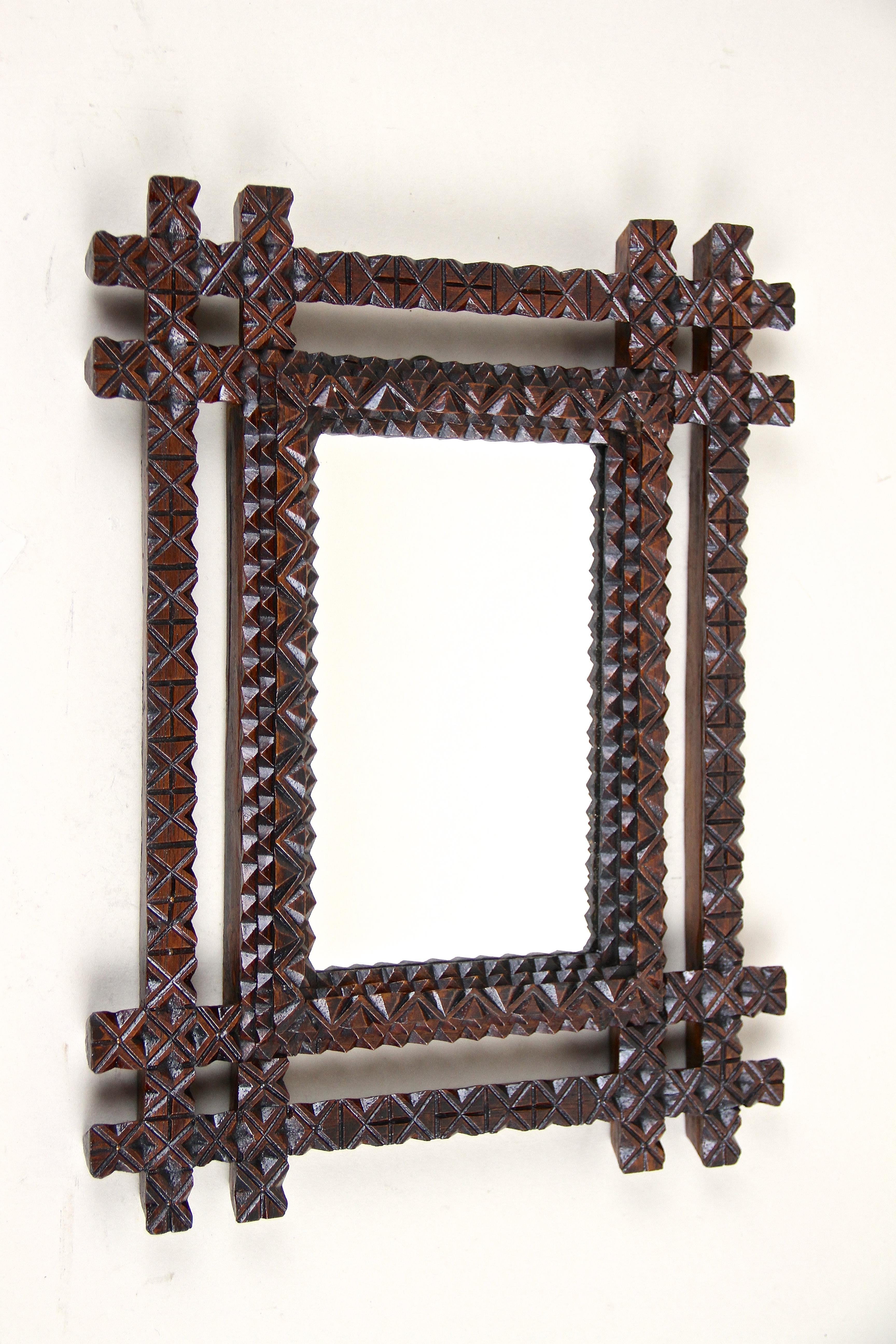 Extraordinary Tramp Art mirror out of Austria from around 1890. A small, stylish mirror with a fantastic rustic flair, effortfully hand carved out of basswood and stained in a dark brown tone. It impresses with a unique carved double bar frame in