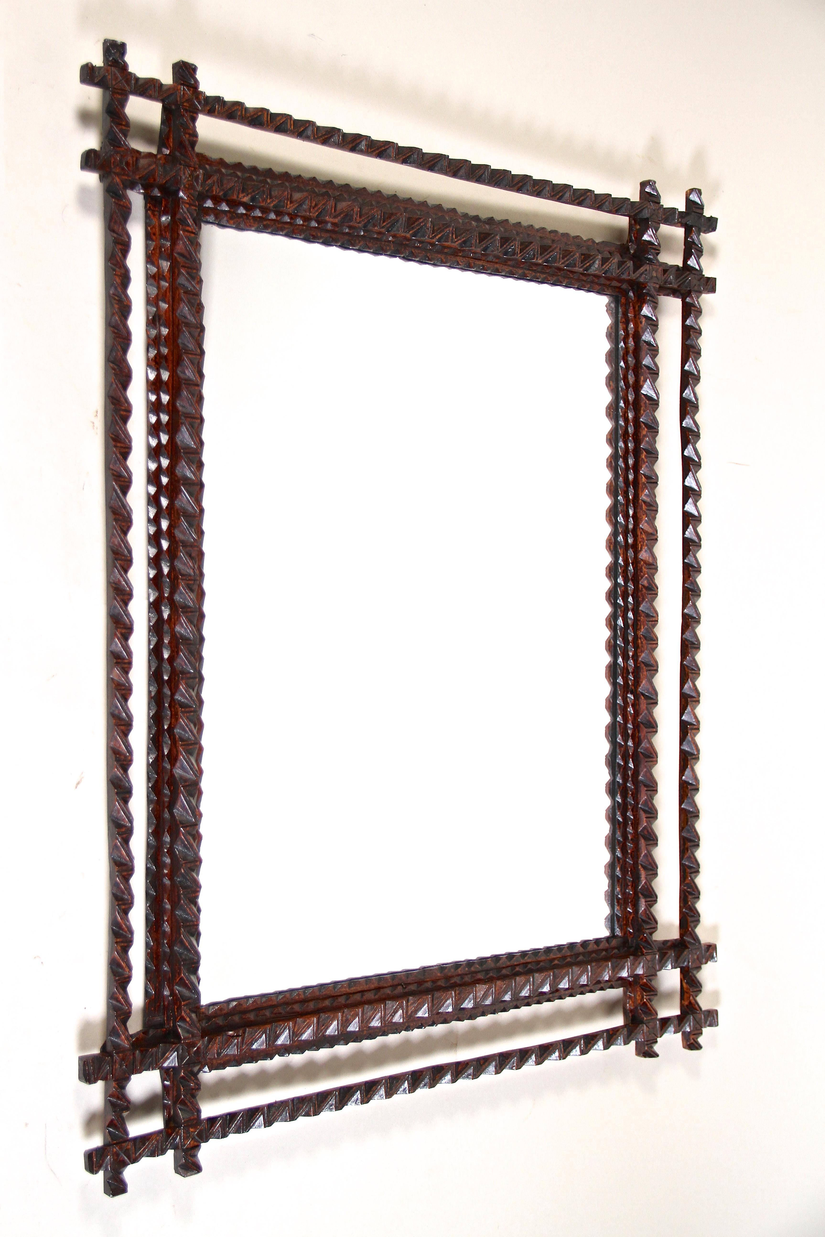 Extraordinary Tramp Art wall mirror from the late 19th century in Austria around 1880. This rustic mirror has been elaborately hand carved out of basswood and comes with a dark brown stained surface in perfect original condition. Highlighted by a