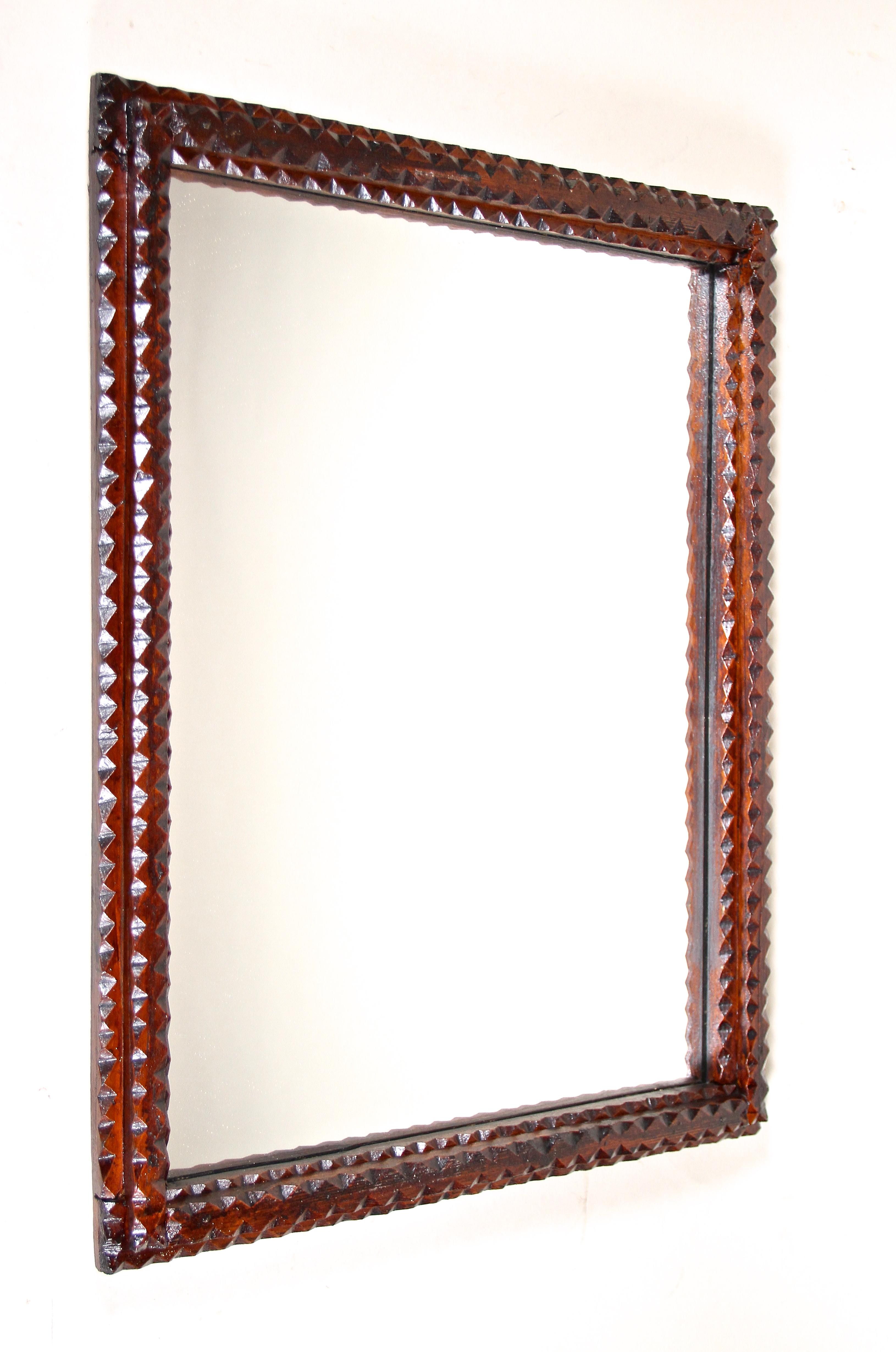 Late 19th century rustic Tramp Art mirror out of Austria from around 1880. The hand carved basswood frame shows lovely chip carvings which confers this highly demanded kind of mirror an unusual rural look. Stained in a beautiful dark brown tone this
