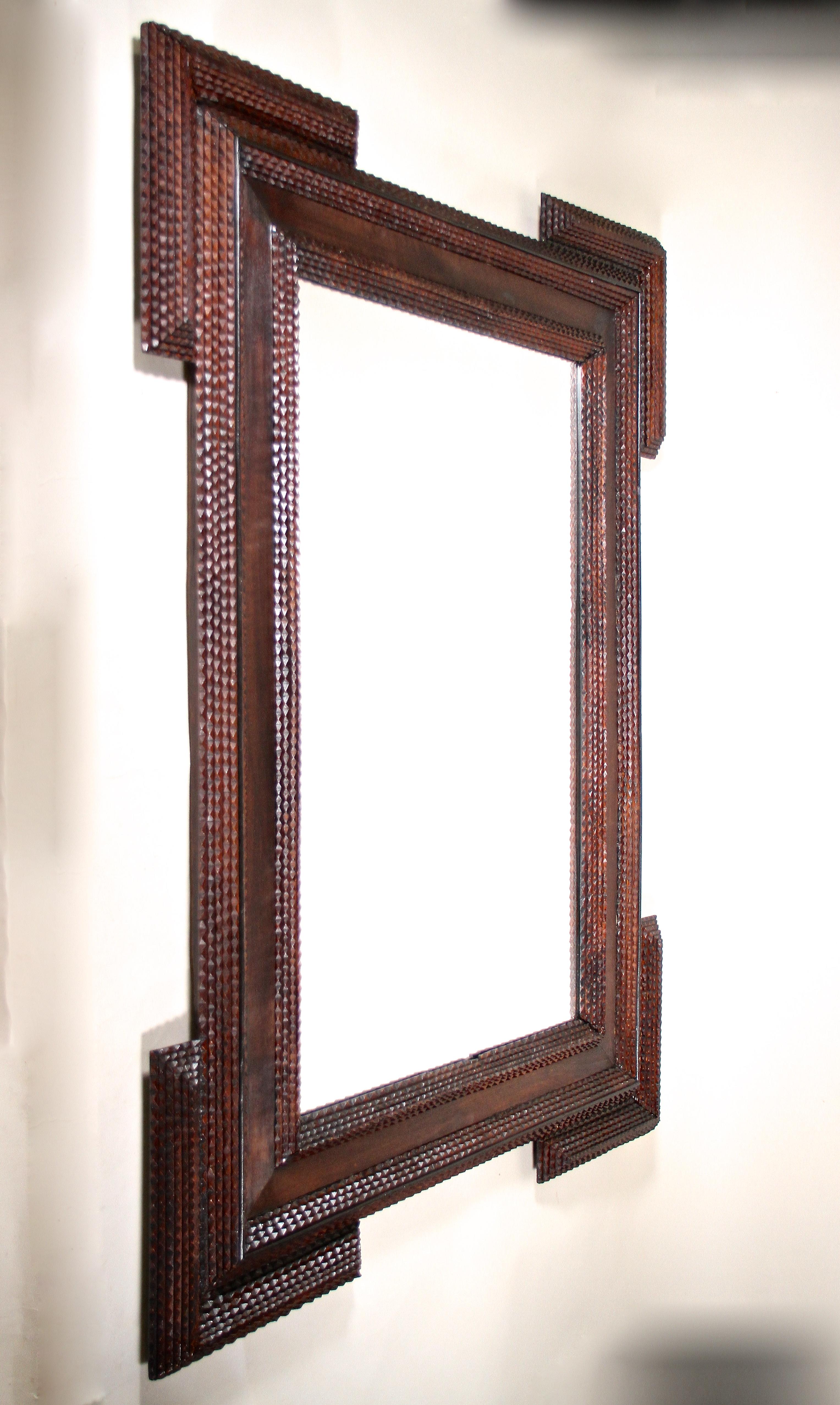 Stunning Rustic Tramp Art wall mirror out of Austria from the late 19th Century around 1880. This large hand carved mirror impresses with an unusually wide frame which is adorned by elaborately worked chip carvings. The protruding corners show a