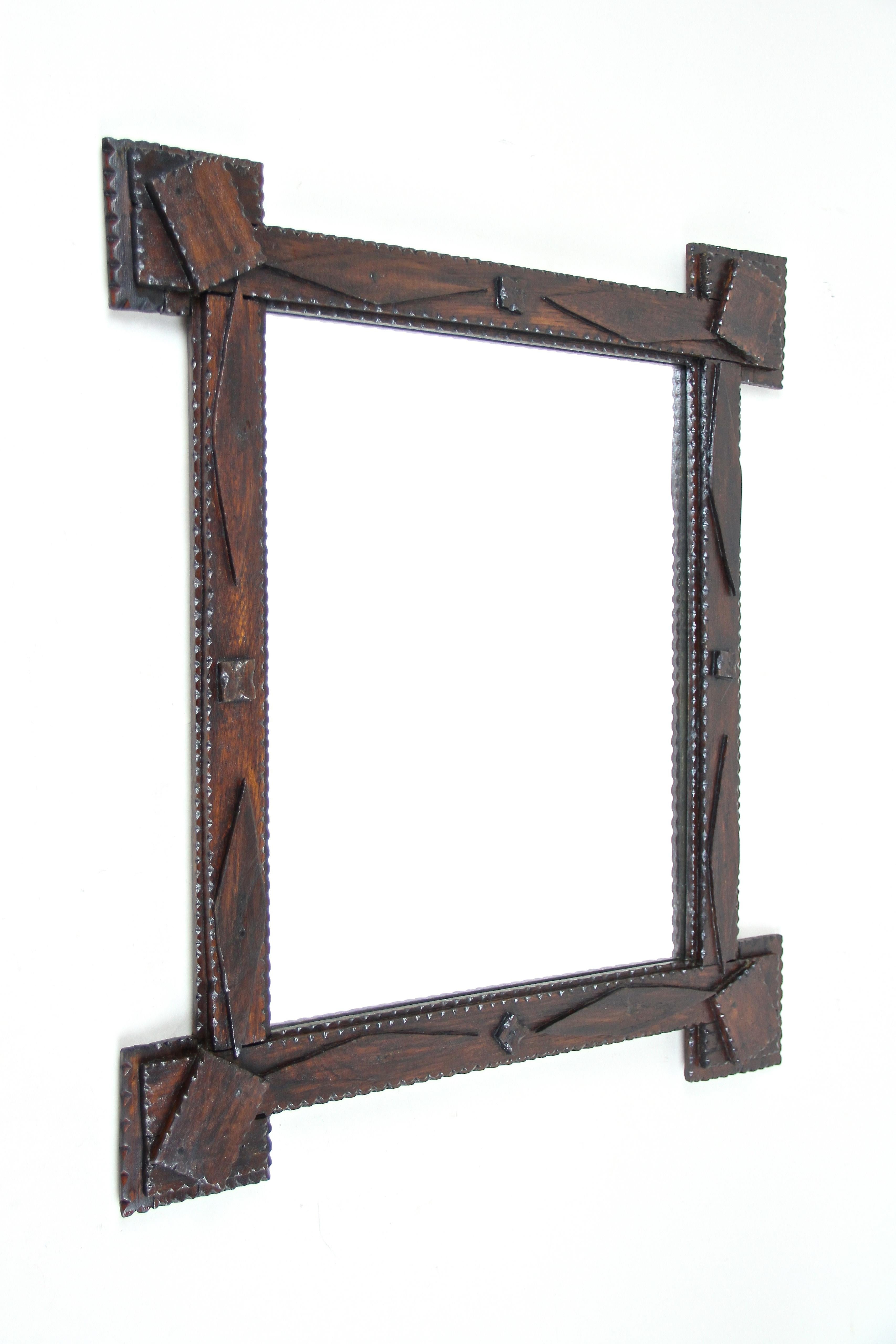 Uncommon rustic tramp art wall mirror from the late 19th century in Austria, around 1870. The beautiful shaped frame was stained in a nice dark brown and shows extended corners with a very unusual design: the last plate of this so-called 