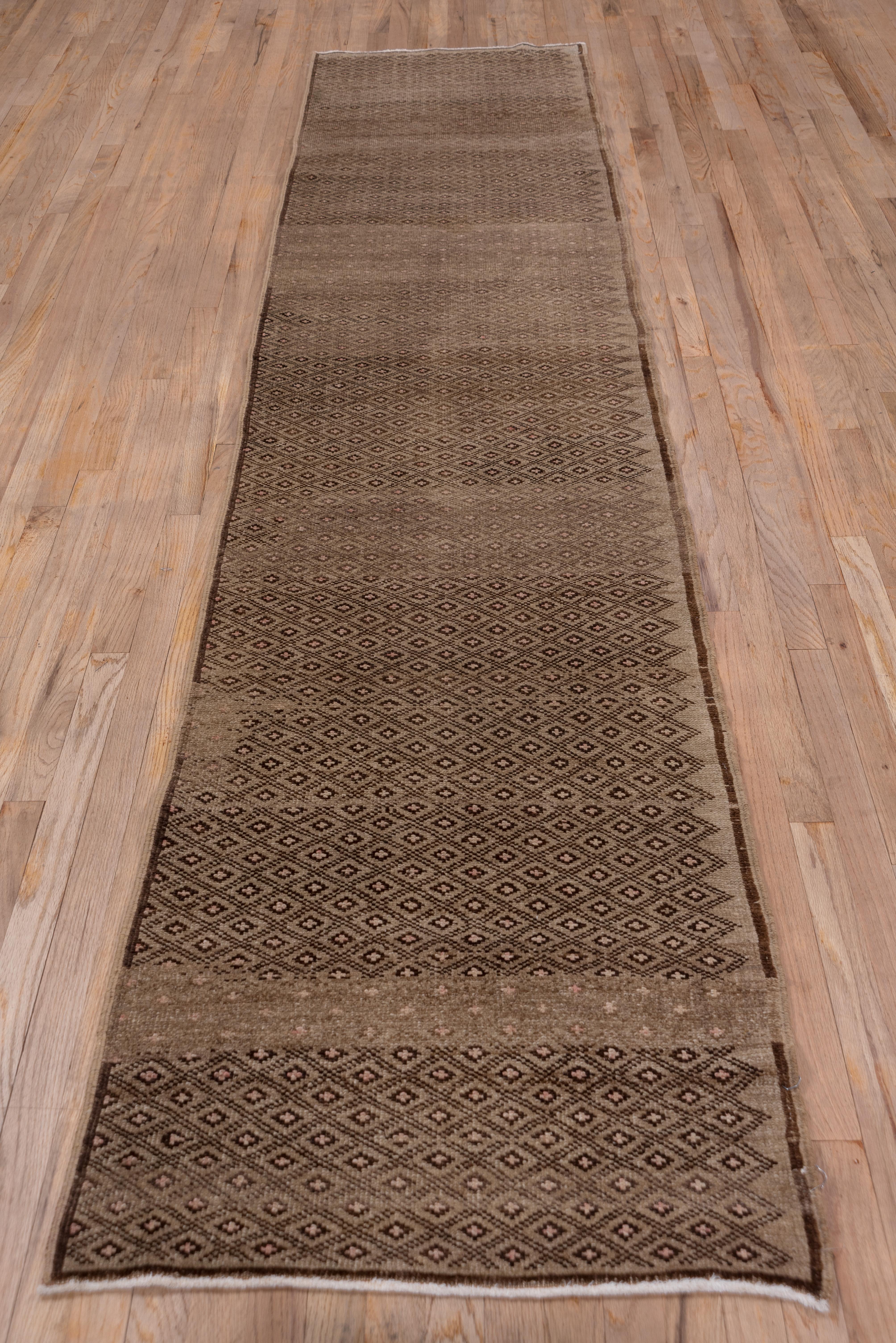 Both the narrow string plain brown border and the light brown field are simultaneously abrashed in this good condition central Turkish rustic runner. The doubly line lozenge lattice encloses small dark brown and ivory devices. The lattice and the