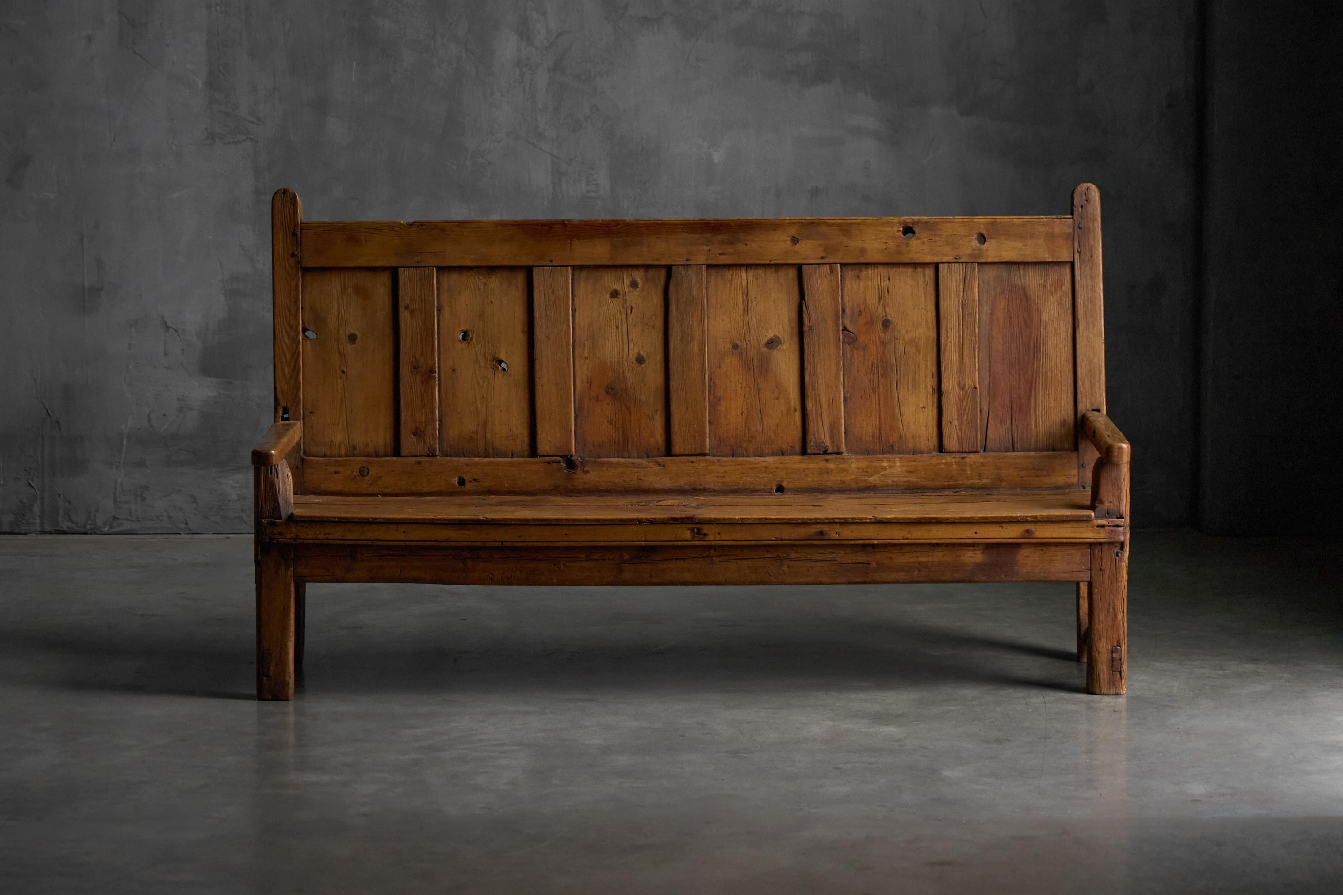 A beautifully preserved rustic bench from 19th-century France, exuding the charm of simple rural craftsmanship. Constructed in solid wood, it features a paneled backrest, sturdy armrests, and a naturally aged patina that highlights its authenticity.