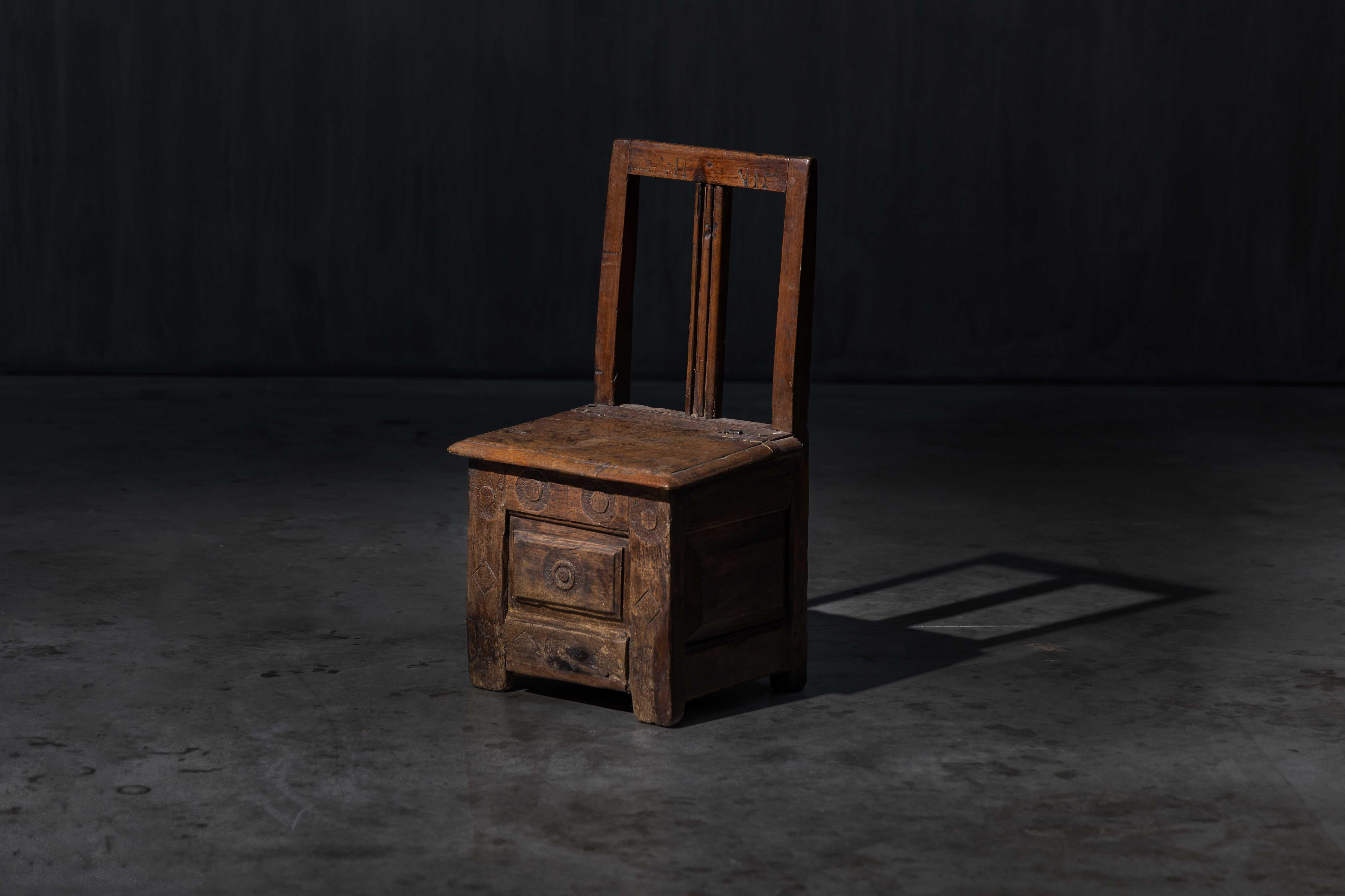 Dieser handgefertigte Holzstuhl verbindet Vintage-Charme mit cleverer Funktionalität und verfügt über ein verstecktes Staufach unter der Sitzfläche. Sein solides, altmodisches Design und die geschnitzten Details machen ihn sowohl zu einem