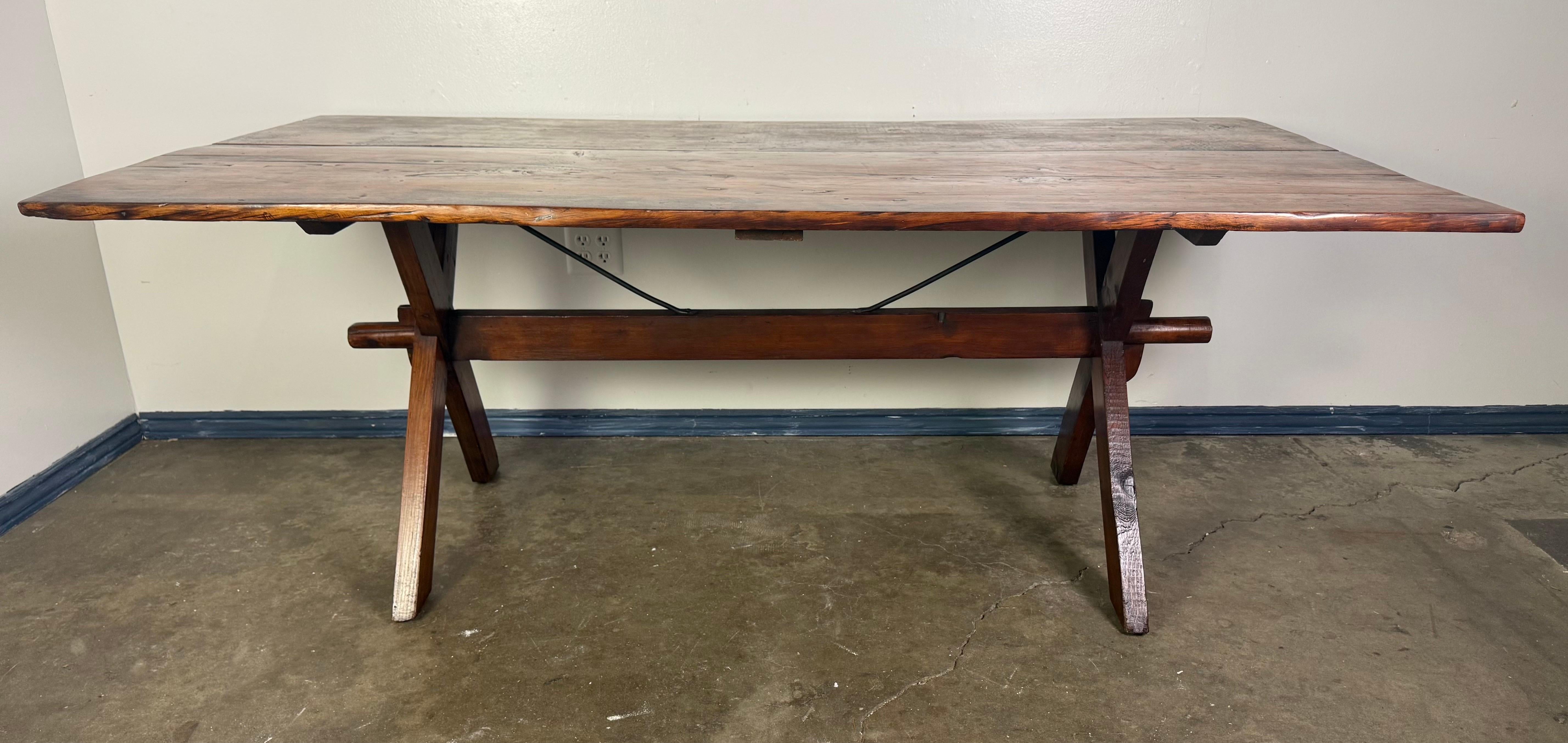 A beautifully worn, handcrafted trestle dining table with timeless rustic appeal, dating to the mid-20th century. The generously sized rectangular top is fashioned from solid wood planks, showcasing natural variations, knots, and a softly weathered