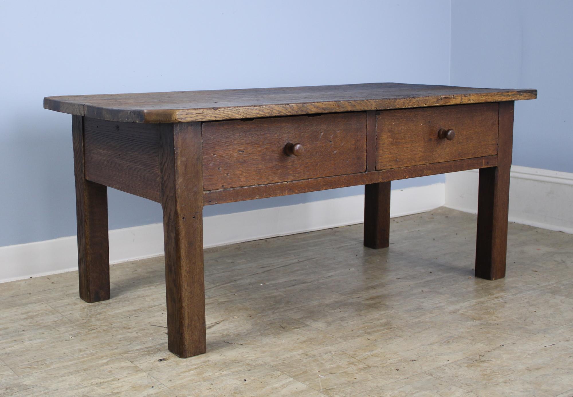 A dark oak coffee table with lots of interesting distress on the top and two roomy drawers. Other details of note are the chunky straight legs and the chamfered corners. Very nice patina and a good country look.