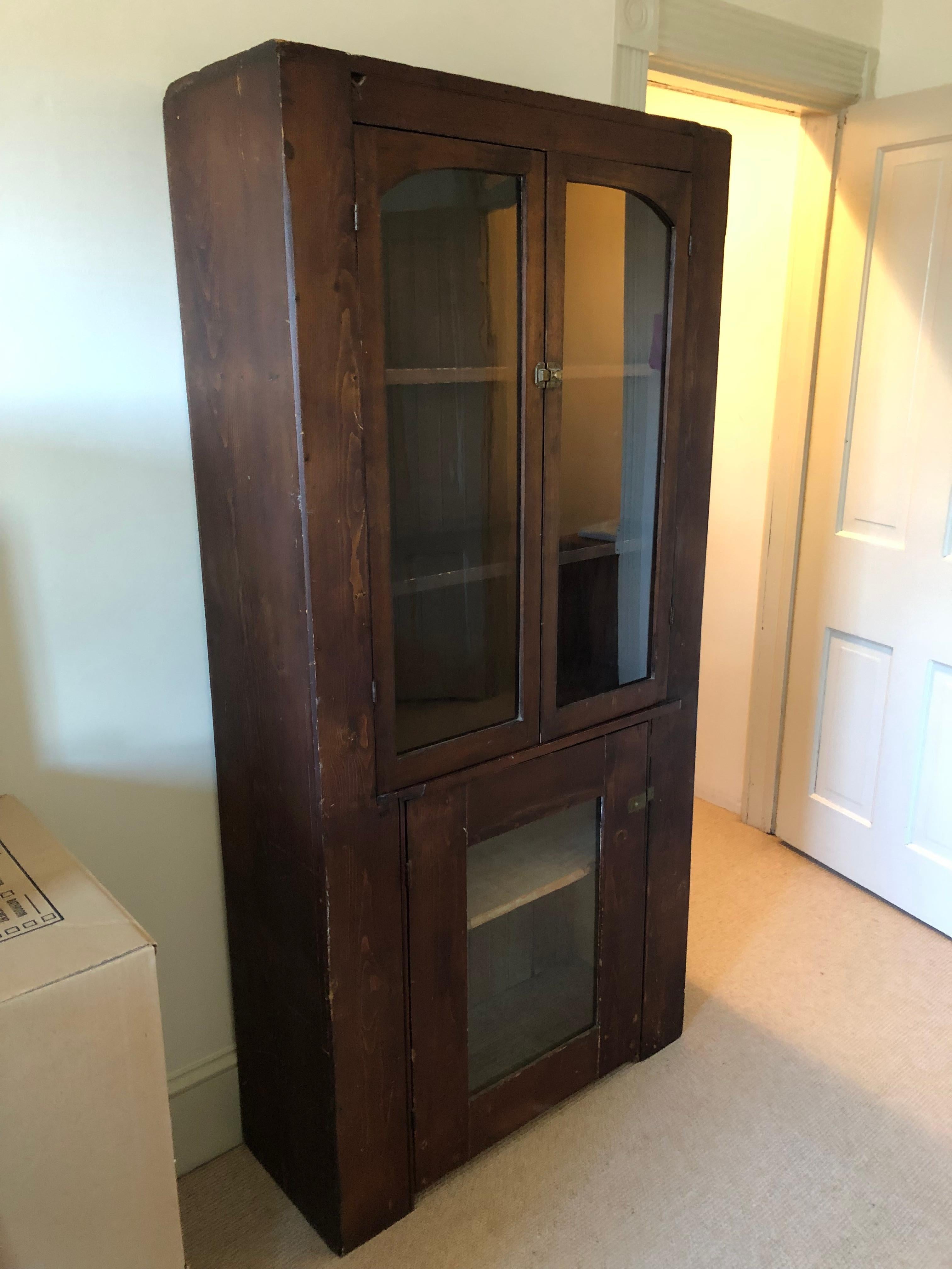 Rich with character, a country style stained wood cabinet having top with two glass doors that open to an interior with 2 shelves that are 11.5 w. 
Bottom has wooden framed single door with glass and interior single shelf. Interior of bottom