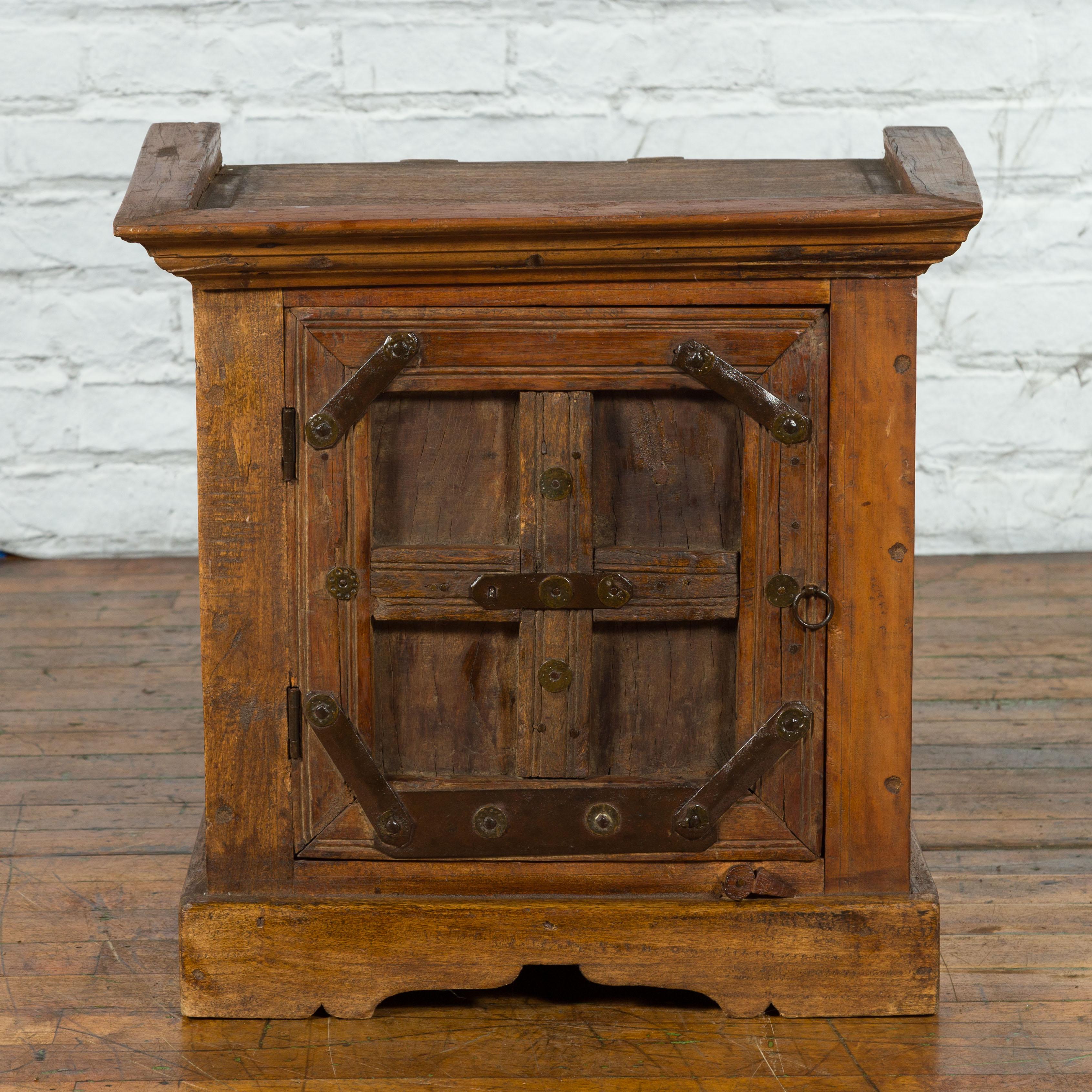 A vintage Indian sheesham wood side cabinet from the mid 20th century with natural finish, single door, iron hardware, scalloped plinth and rustic character. Created in India during the Midcentury period, this rustic small sheesham wood bedside