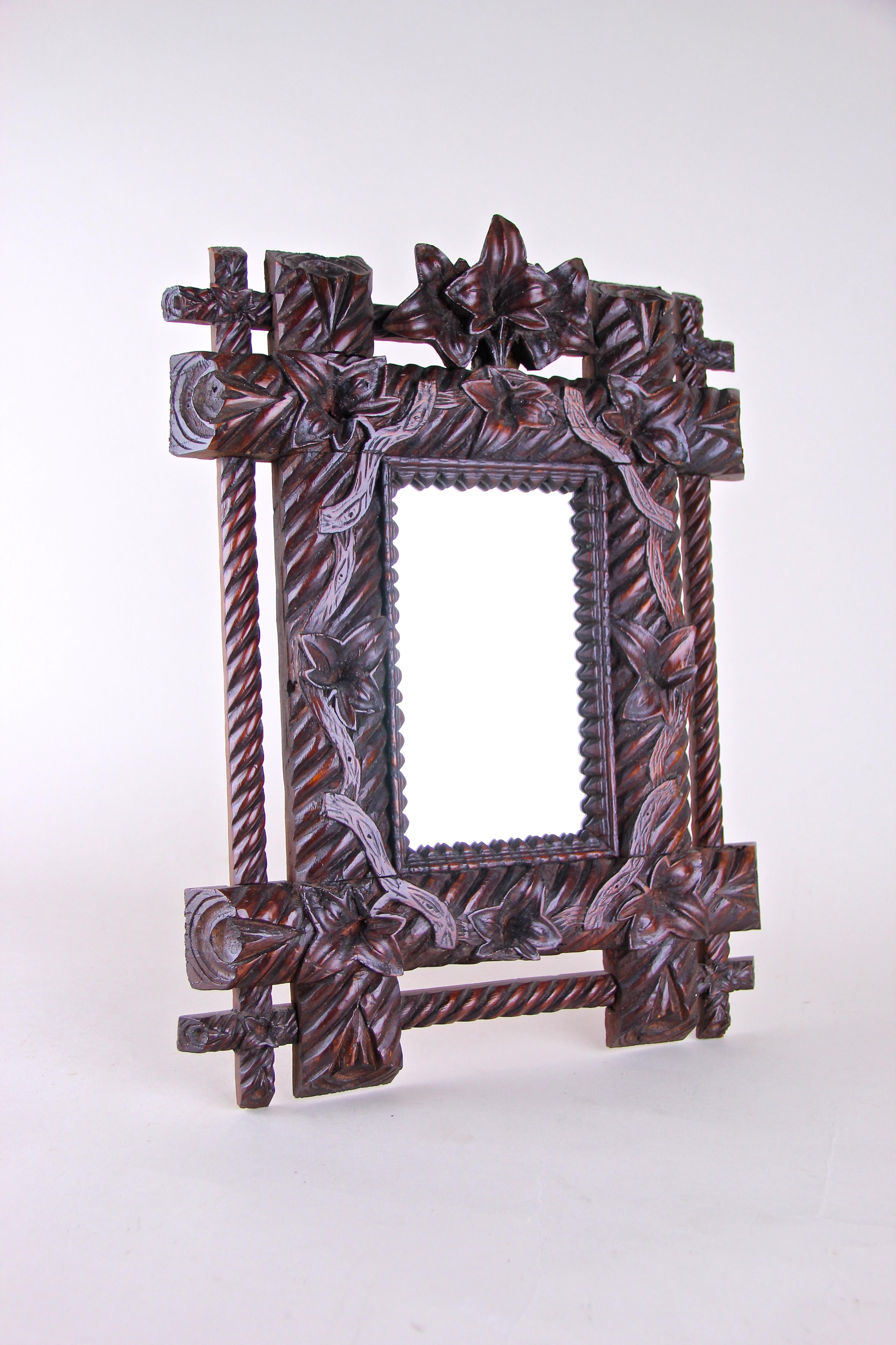 Fancy small rustic Black Forest wall mirror from the late 19th century in Germany around 1880. Hand carved out of basswood, the wide dark brown frame shows a matchless design combined with great worked bellflowers and tendrils. The bulky inner frame