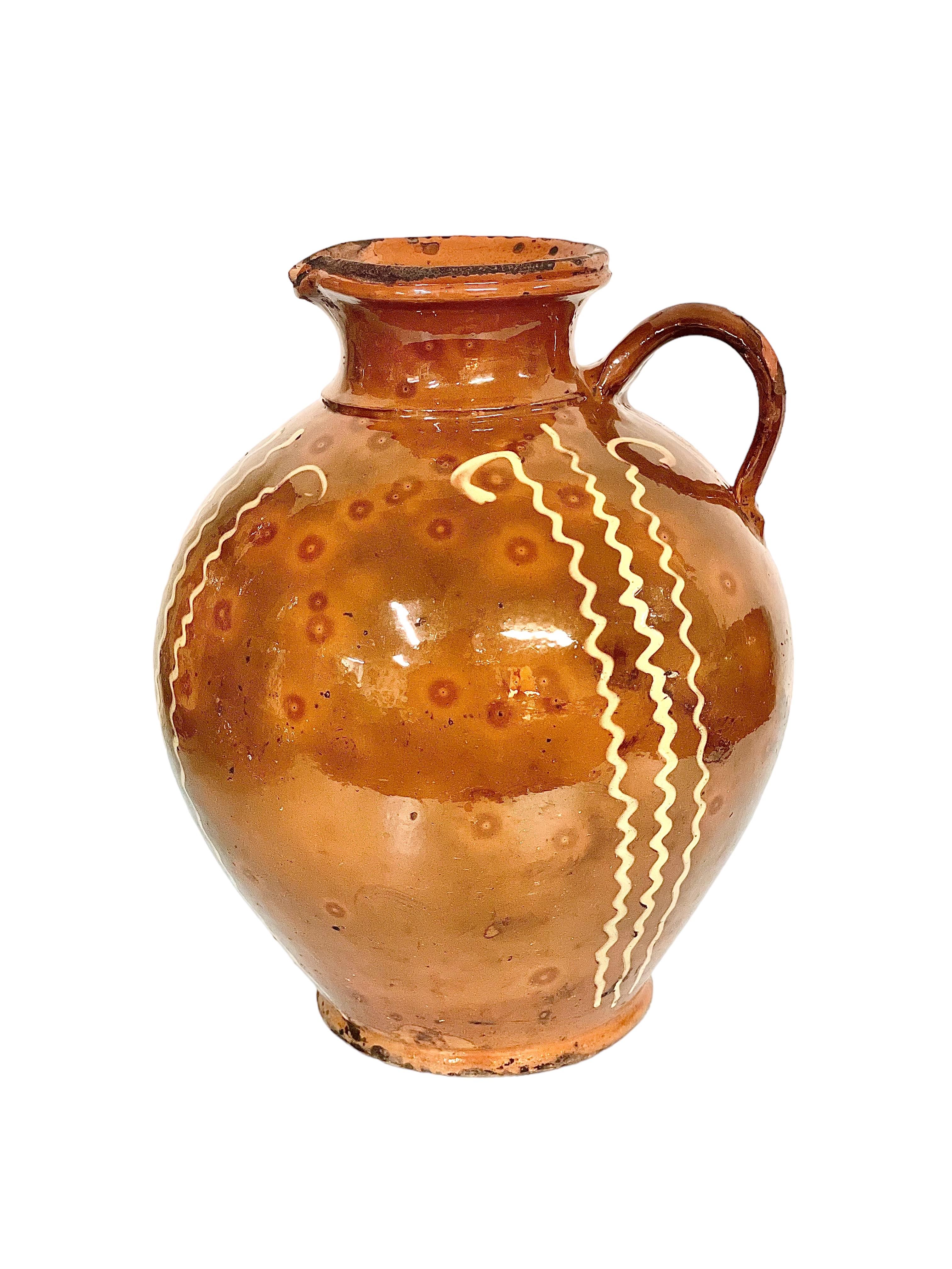 A rustic French pottery jug with handle and shaped spout from the 19th century, in glazed terracotta with a striking, hand-painted design of vertical yellow zig-zags. Originally a piece of utilitarian kitchenware, used for transporting and storing