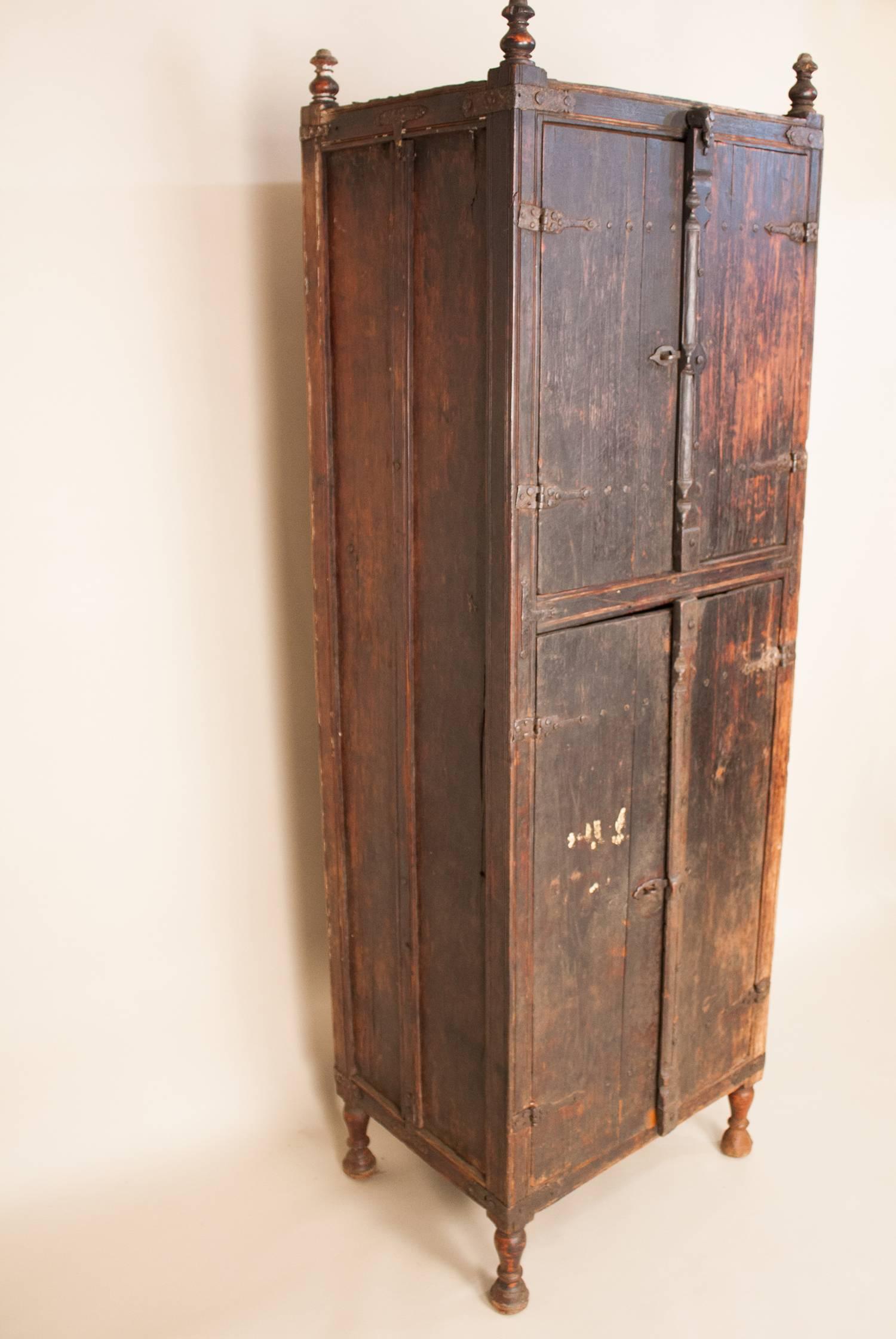 A tall, slender primitive cabinet from Portuguese Goa, circa 1850. This antique cupboard is in its original condition and has smithed iron straps, hinges and hardware, including bent handmade nails, that add great character to the piece. The wood