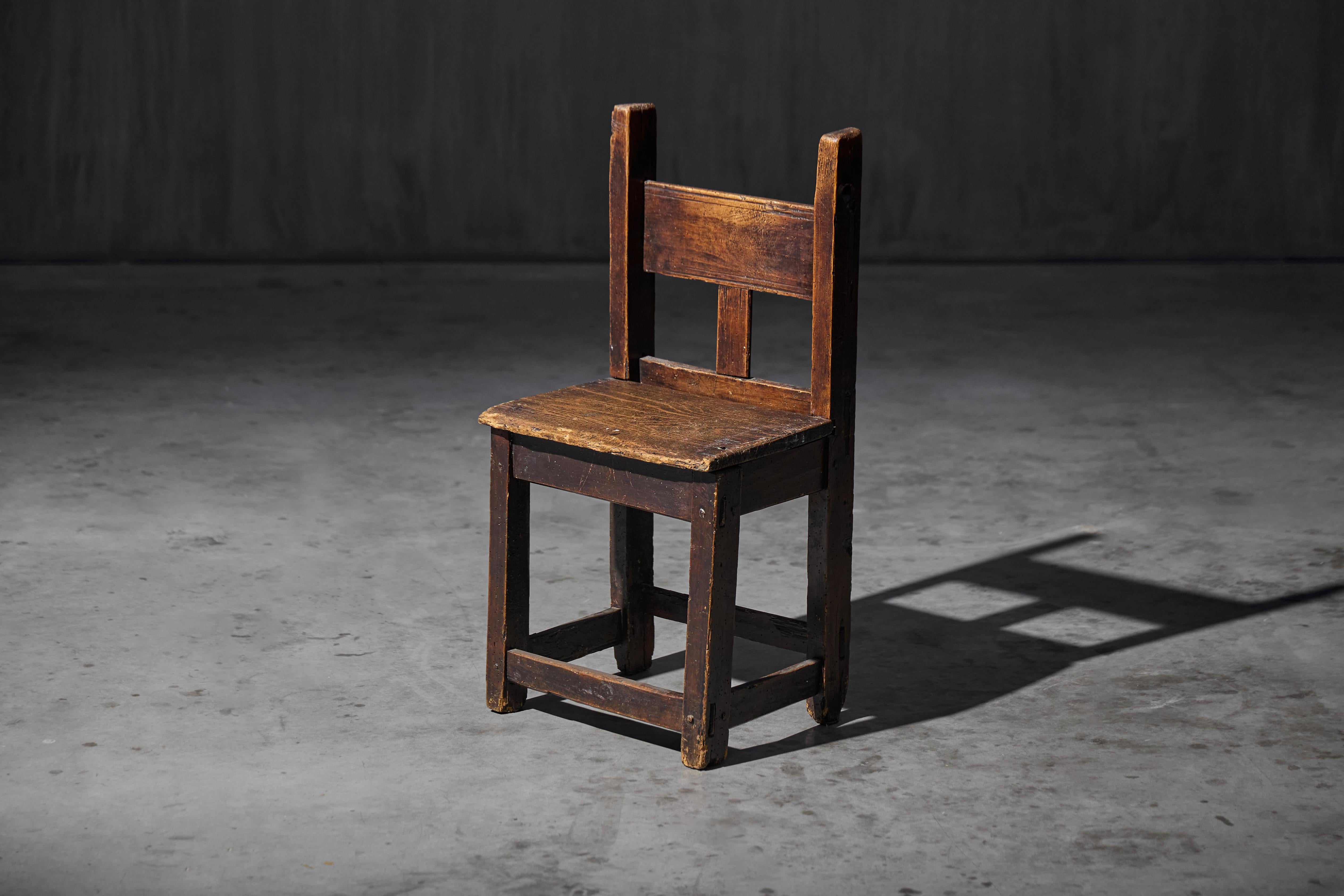 19th century rustic wooden children's chair, crafted from dark solid wood. This minimalist chair brings a touch of historical charm to modern interiors. With its timeless design and sturdy build, it not only provides comfort and style for your