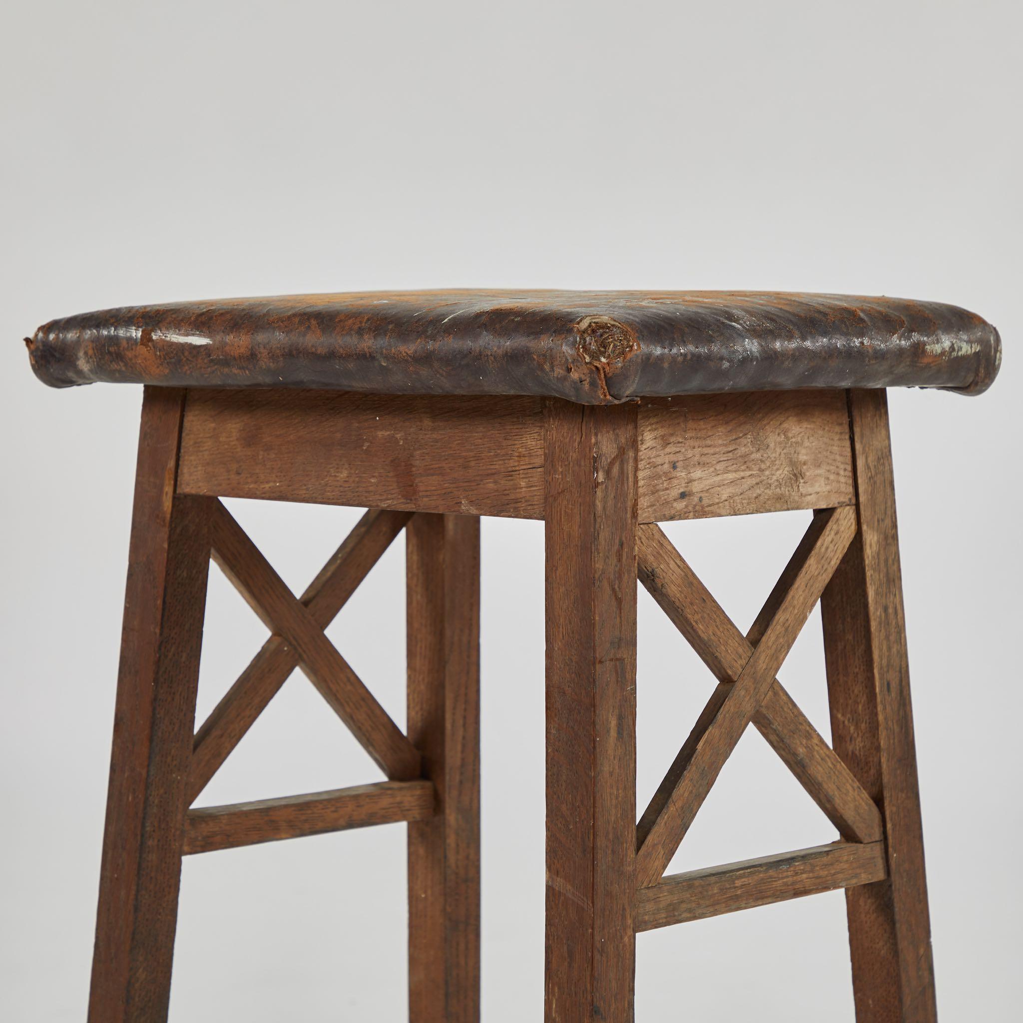 Early 20th-century English wood stool with square leather top, two X-shaped stretcher accents and a footrest on all sides. A rustic piece with great versatility. 

England, circa 1900

Dimensions: 18.5W x 14D x 30H