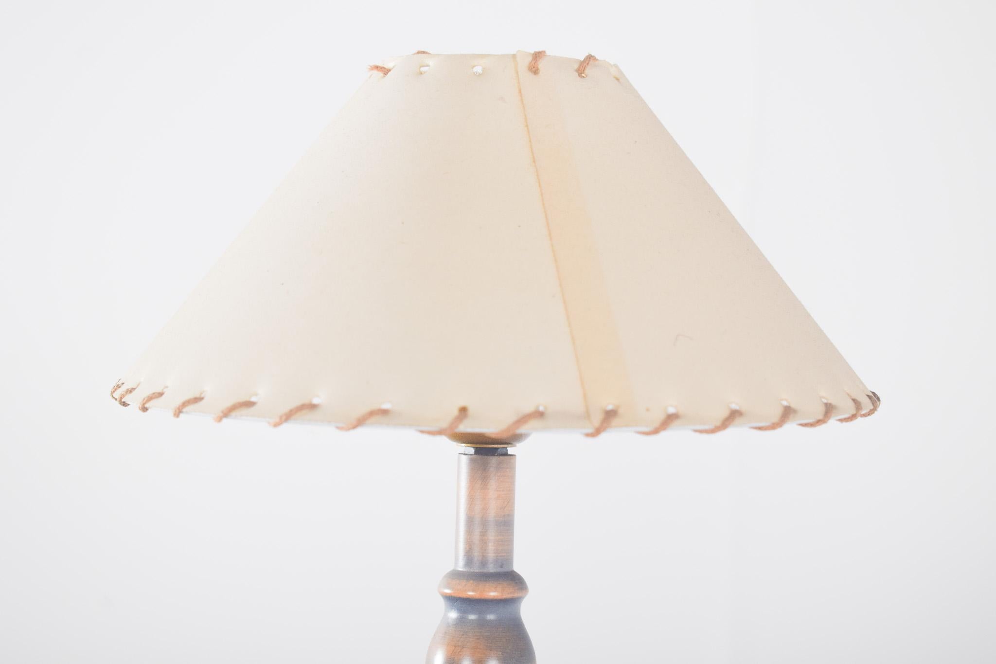 Wooden table lamp. With a rustic and elegant design, it has a turned foot that displays an ornamental twist, creating a dynamic visual effect. The wood is painted in aged shades of blue and gold
The rounded base ensures stability and follows the