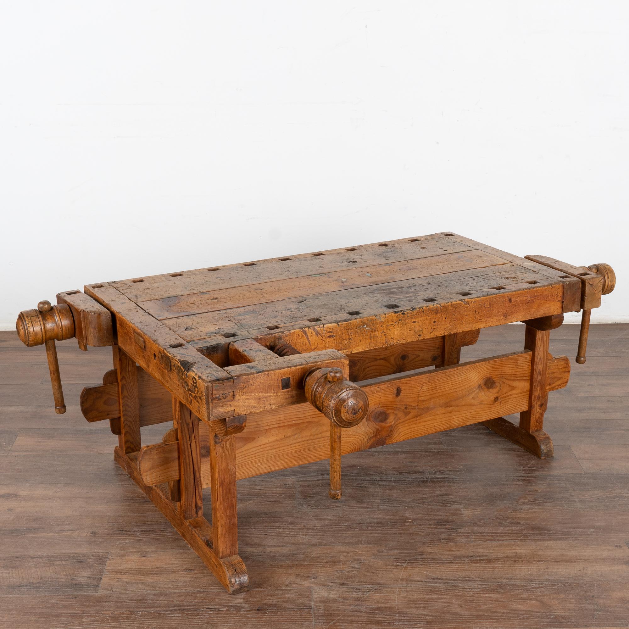 This rustic coffee table is a rare find. It was formed from a large, old carpenter's workbench and scaled down to coffee table height. 
It is the years of constant use revealed in every ding, gouge, cracks, old dried worm hole and stain that enrich
