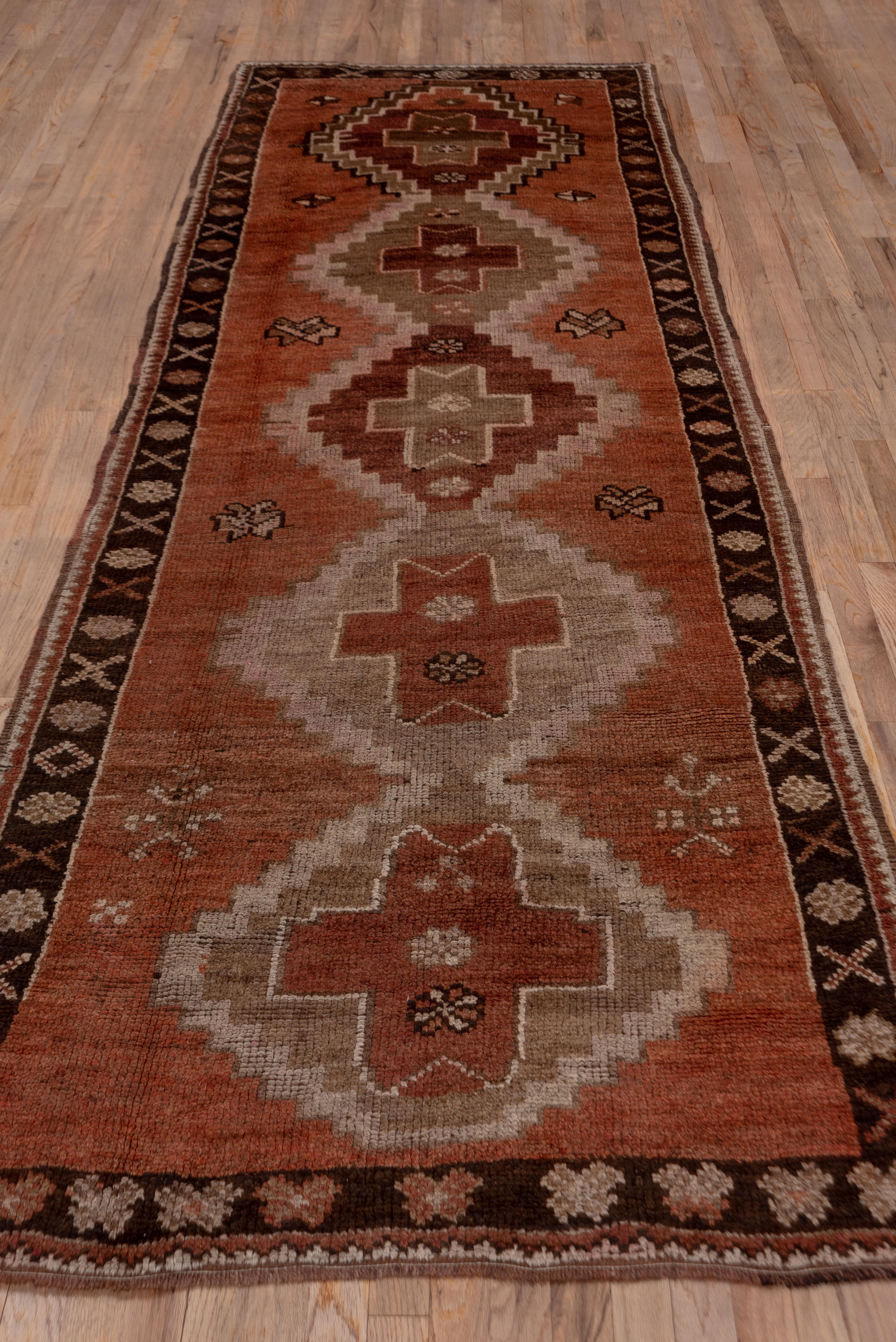 The coral red field of this Northeast Turkish rustic long rug displays five stepped medallions in red, pale green and light coral.