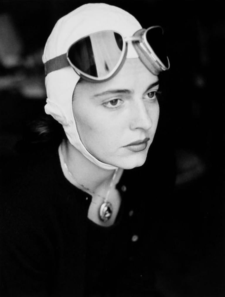 Jinx in Goggles, Florence, Italy by Ruth Orkin is a black and white portrait of a woman, wearing goggles with a white cap underneath. This photograph is part of Orkin's series, American Girl in Italy. 

Open Edition
Blind stamp on print