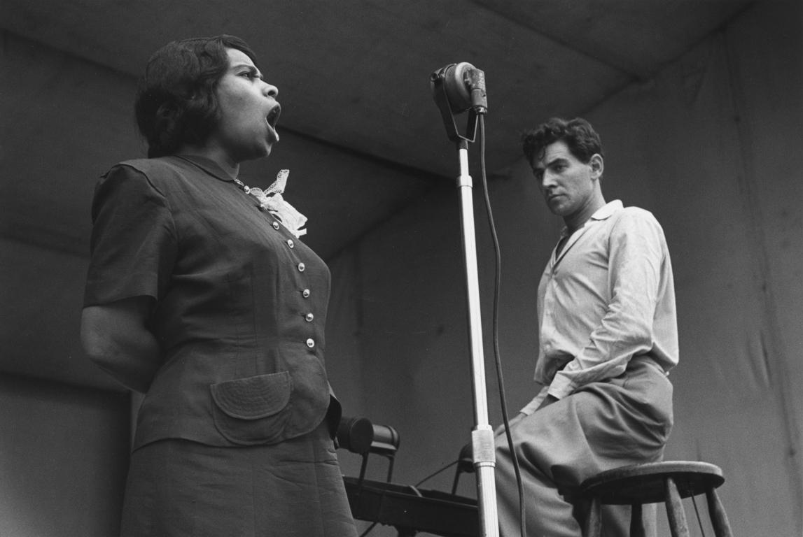 Marion Anderson y Leonard Bernstein, Lewisohn Stadium, NYC por Ruth Orkin representa a un hombre y una mujer actuando en el escenario. Marion Anderson está de pie con los brazos a la espalda, el rostro tenso por la concentración mientras canta al