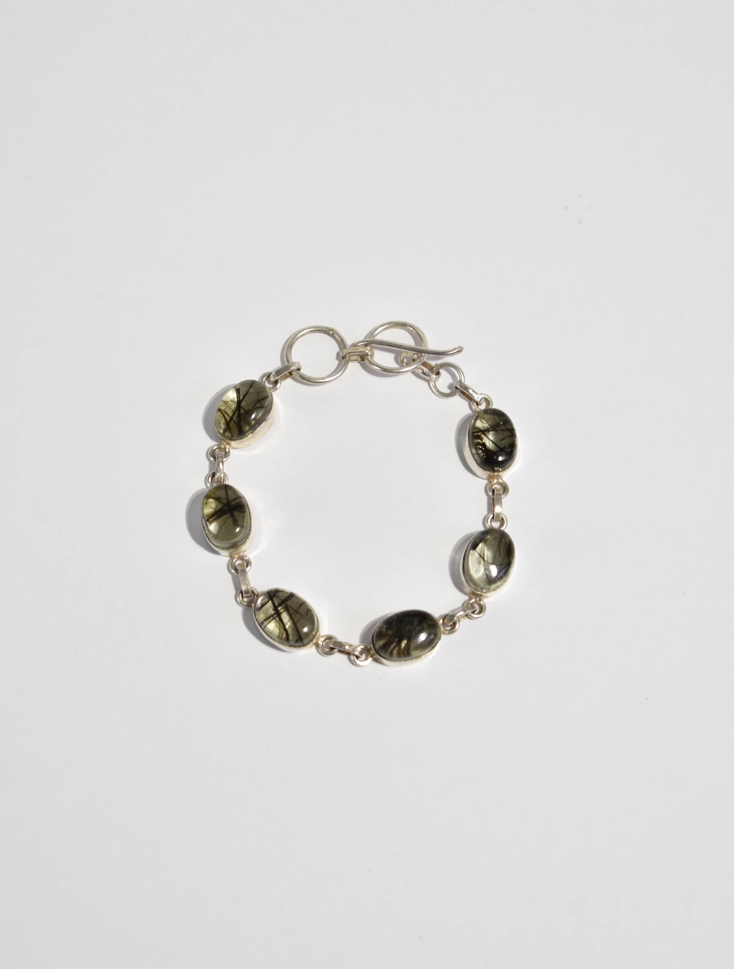 Beautiful vintage sterling bracelet with bezel set oval rutilated quartz cabochons and toggle closure, stamped 925.

Material: Sterling silver, rutilated quartz.