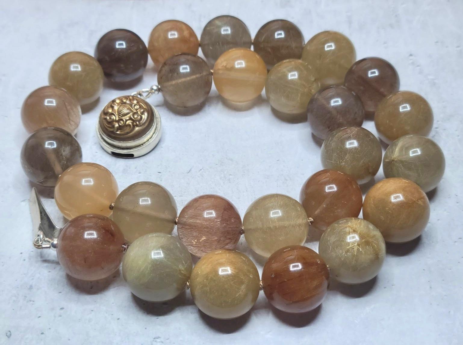 We are excited to present our addition to the collection - a stunning Rutilated Quartz necklace. Measuring 22 inches (56 cm) in length, this necklace is made of smooth round beads (20mm) in a rich reddish-brown, caramel, gold, and silky pink color.