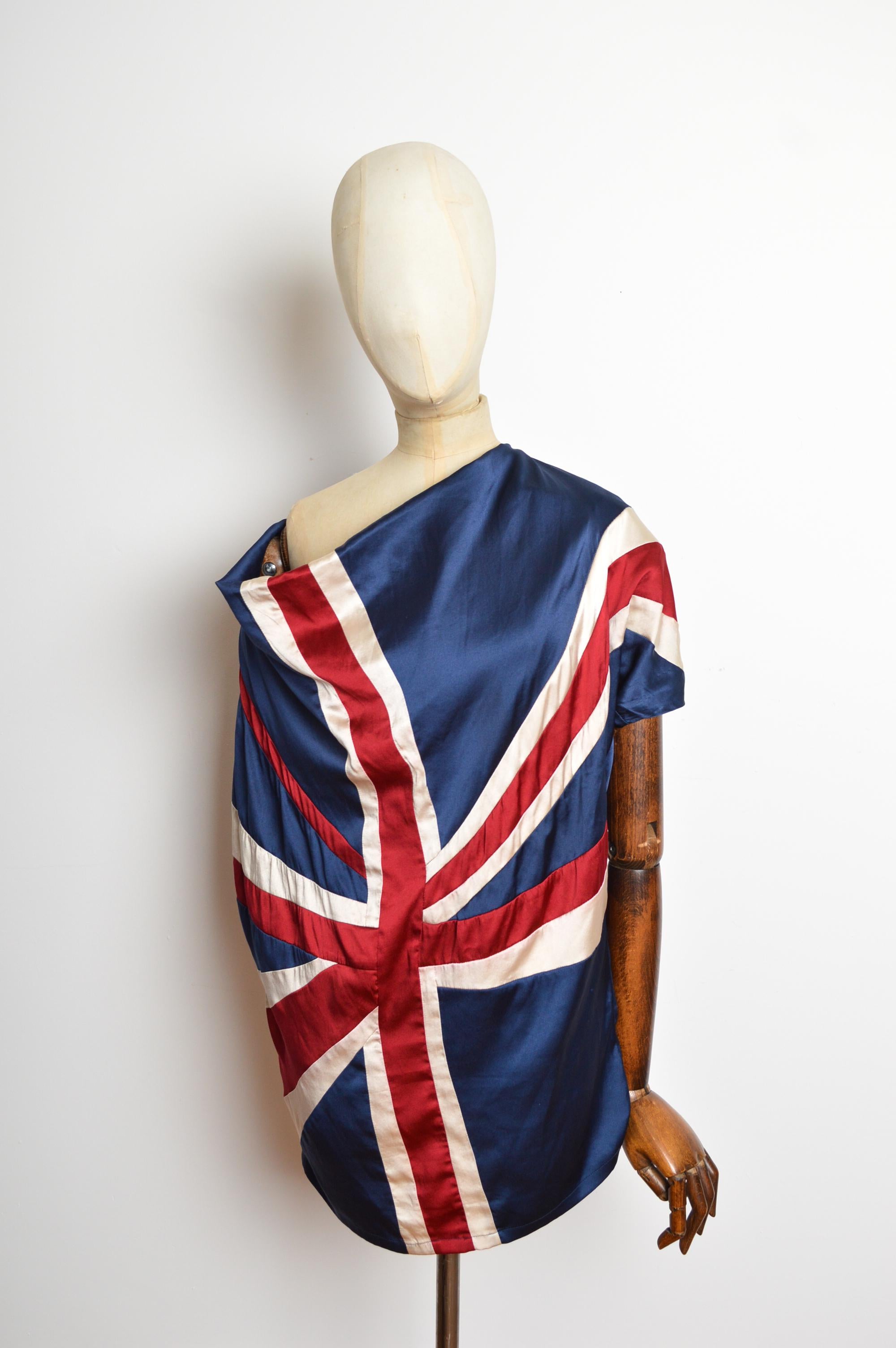 Una tunica Union Jack anni 2000, giocosa e chic, realizzata in 100% pura seta nei colori navy, avorio e rosso cremisi. Caratterizzato da colletto drappeggiato, maniche corte e orlo lungo fino ai fianchi. 
Susanne Rützou si è diplomata come stilista