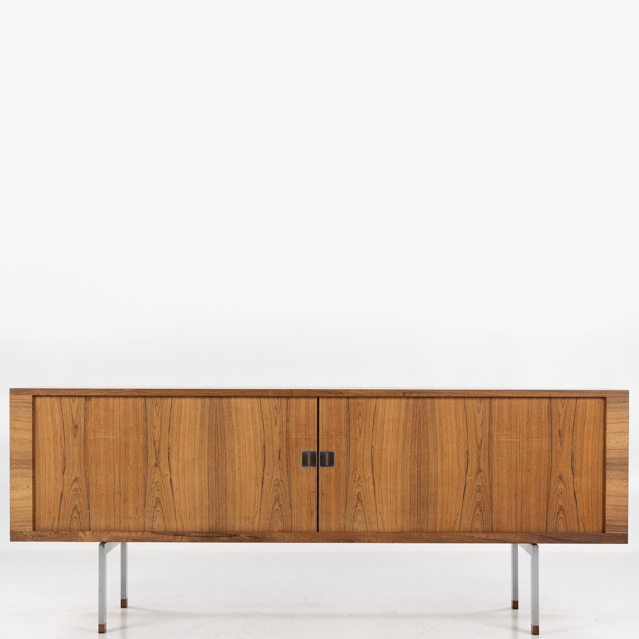RY 25 - Steele in palissandro Rio chiaro con ante a persiana e gambe in acciaio con scarpe in palissandro. Timbro del produttore.
Disegnato da Hans J. Wegner e realizzato da Ry Møbler.