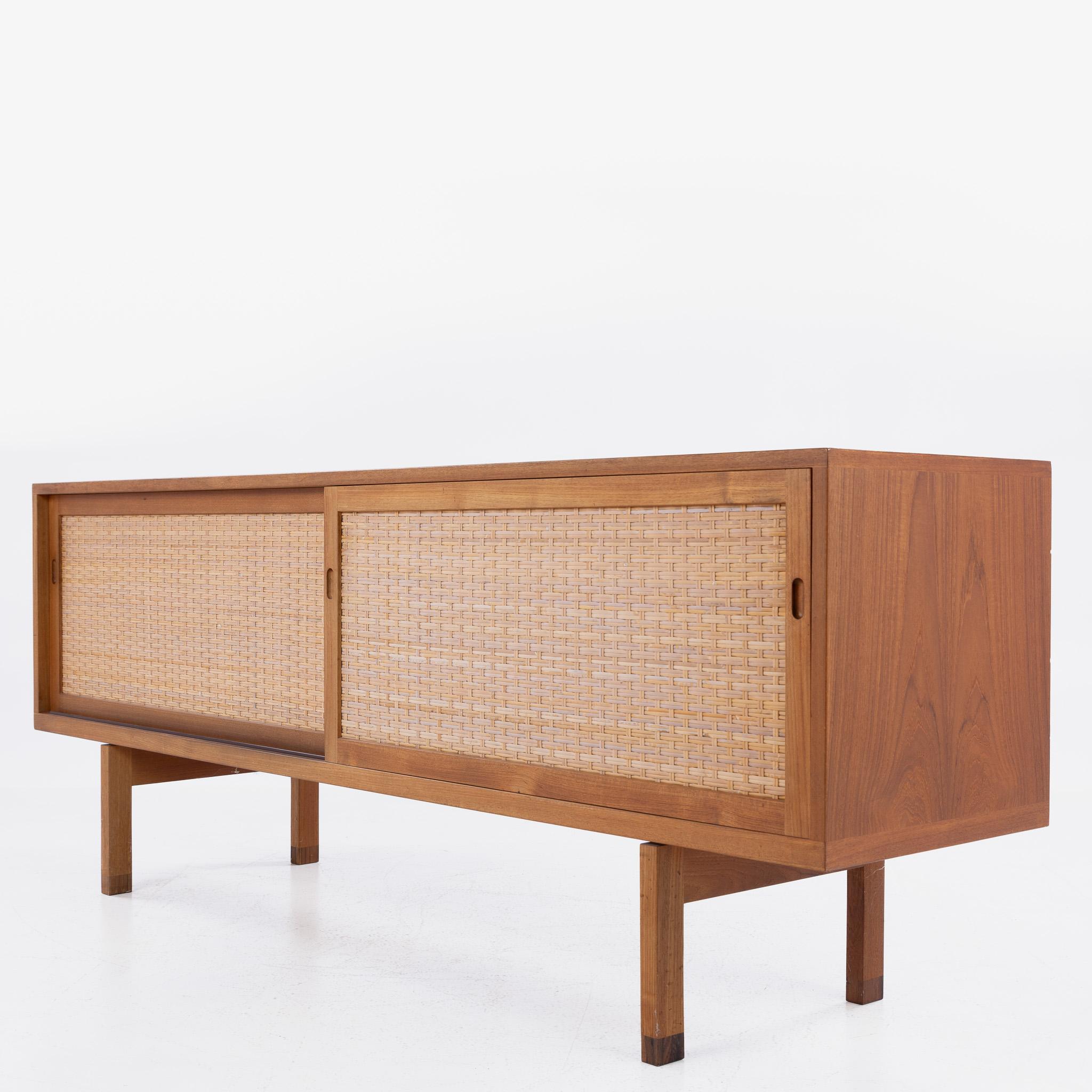 RY 26 - Sideboard in teak with two sliding doors in patinated wicker and rosewood shoes. Designed by Hans J. Wegner.