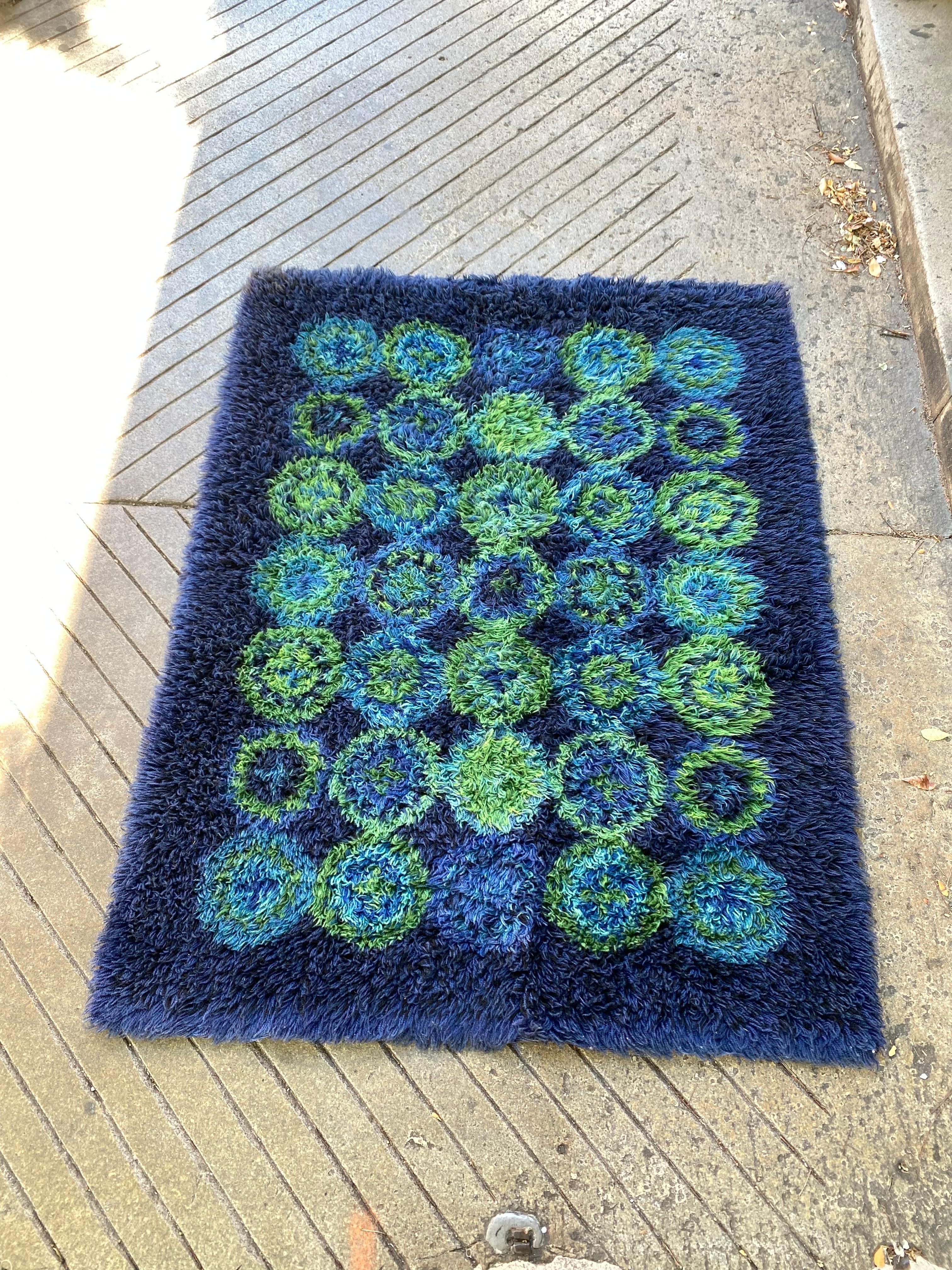 Tapis Rya en bleu et vert.  Les couleurs vives sont toujours aussi belles !  Le tapis n'est pas du tout usé !  Le verso présente quelques décolorations.  Les reliures en toile sont encore en place à chaque extrémité.