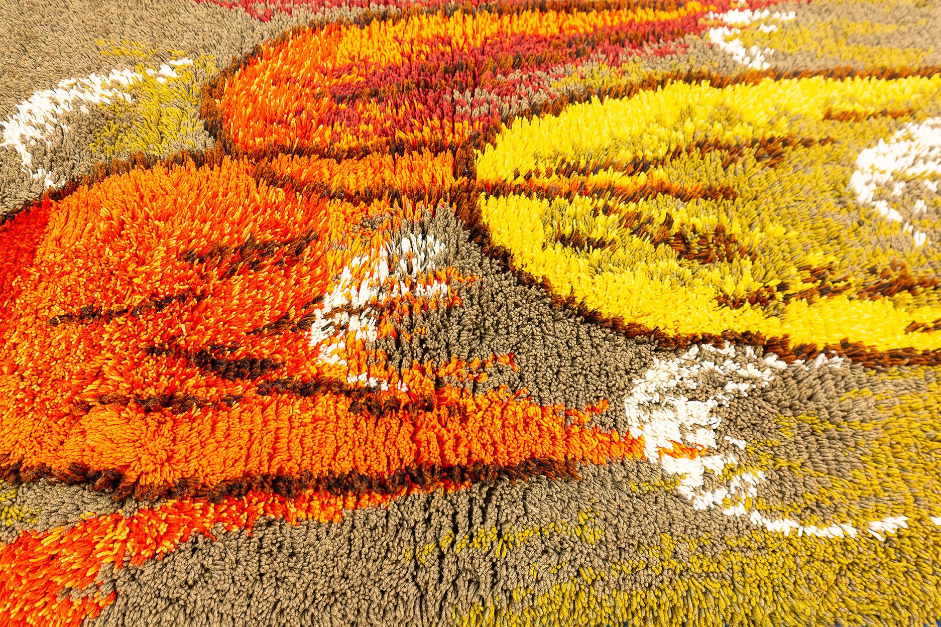 Questo tappeto vintage di Rya, che misura 158 x 107 cm, emana un'energia vibrante e dinamica grazie alla sua audace palette di colori e al suo design astratto. Il pelo profondo della tecnica Rya crea una texture lussuosa, mentre gli arancioni