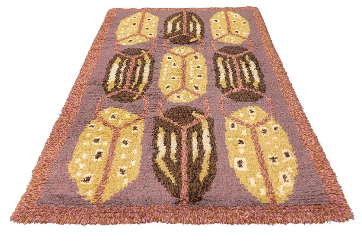 Vintage Scandinavian Rya Rug – Geometric Beetle Motif – 197 × 117 cm
This striking mid-century Rya rug features a unique geometric design reminiscent of stylized beetles or shields, set against a muted mauve-lavender ground. Rich golden yellows,