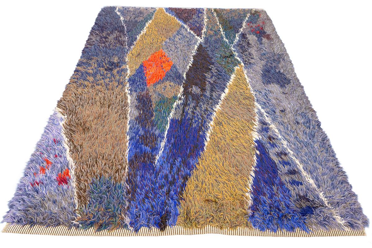 This exceptional Rya rug, featuring an abstract design, is a true testament to Scandinavian textile artistry. The composition is alive with dynamic movement, created through sharp, angular forms and a palette that bridges deep earth tones and vivid