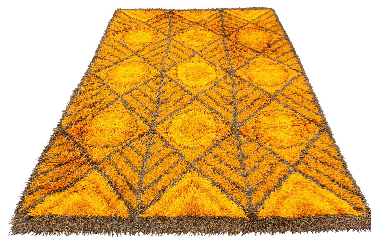 Questo straordinario tappeto scandinavo Rya, che misura 197 × 140 cm, è un superbo esempio di design tessile nordico della metà del XX secolo. Tessuto con una spessa trama di lana a pelo alto, questo pezzo esemplifica la classica tecnica di