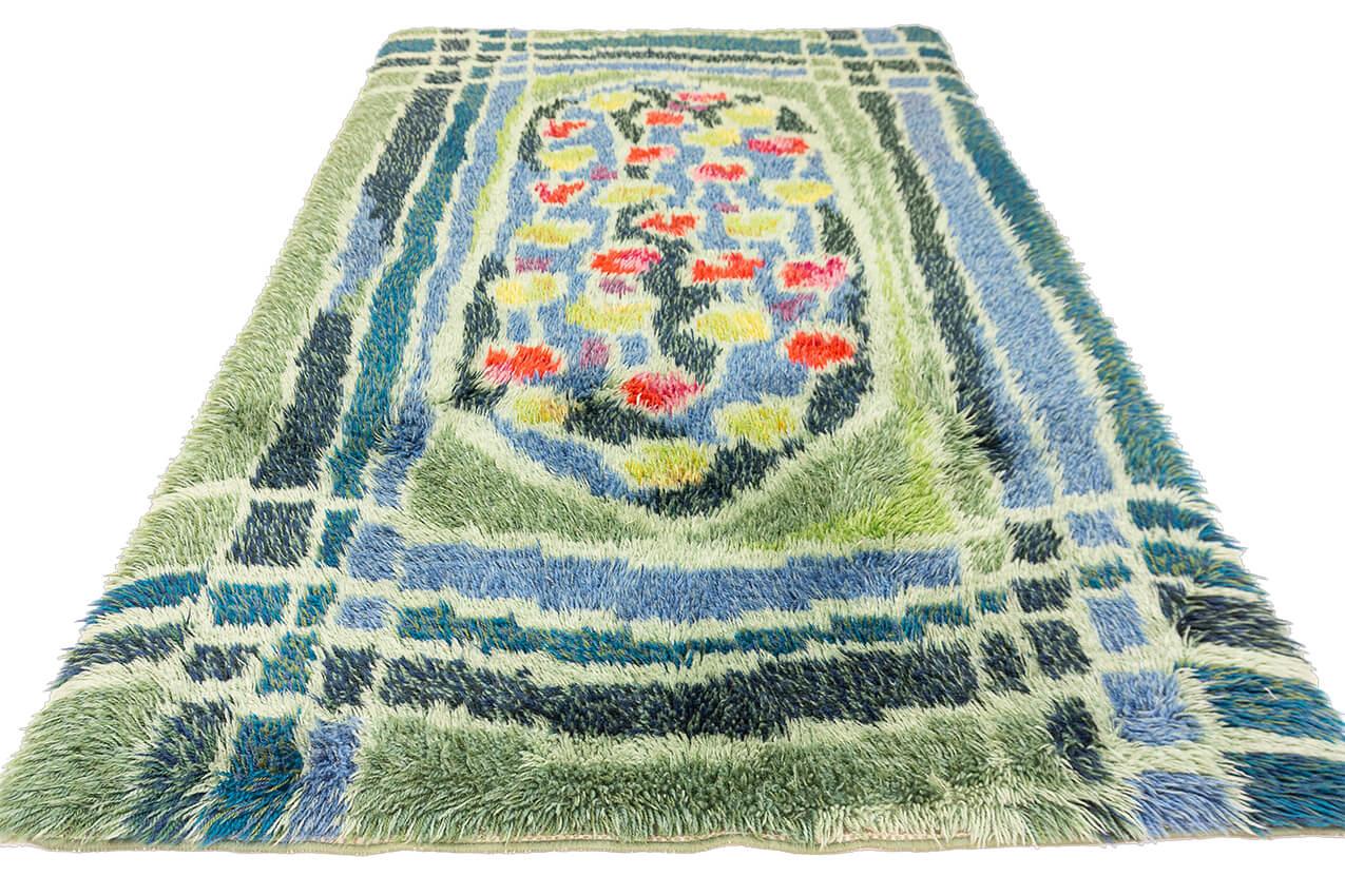 Verwandeln Sie Ihren Wohnraum in eine ruhige Oase skandinavischen Charmes mit unserem schwedischen Teppich Rya in üppigem Grün und beruhigenden Blautönen. Dieser Teppich ist eine harmonische Mischung aus von der Natur inspirierten Farben und