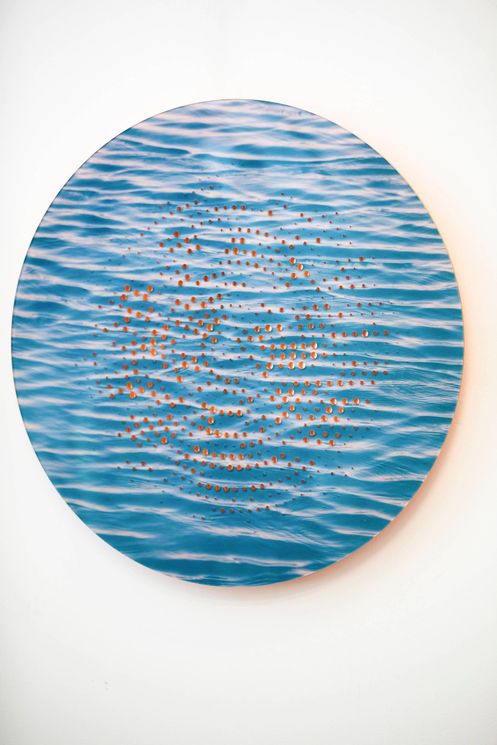 Una stampa a pigmenti di onde blu illuminate dal sole è traforata da un brillante disegno concentrico arancione in questo tondo di Ryan Van Der Hout. Il preciso design tagliato al laser si illumina di luce arancione e riflessa, rivelando gli strati