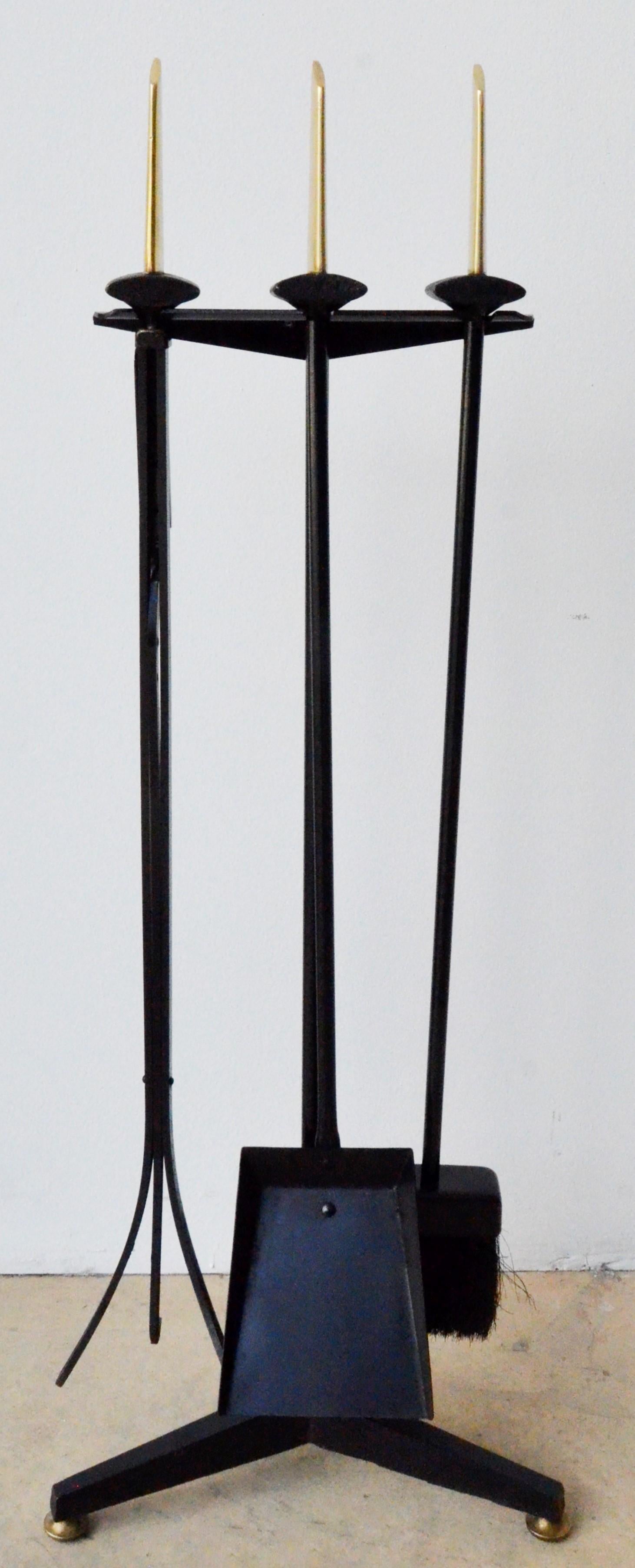 Offered is a set of four (three tools and holder) Mid-Century Modern Donald Deskey black wrought iron with brass handles three fireplace tools with stand. The offered fireplace set was designed and manufactured during the 1950s. The brass handles at