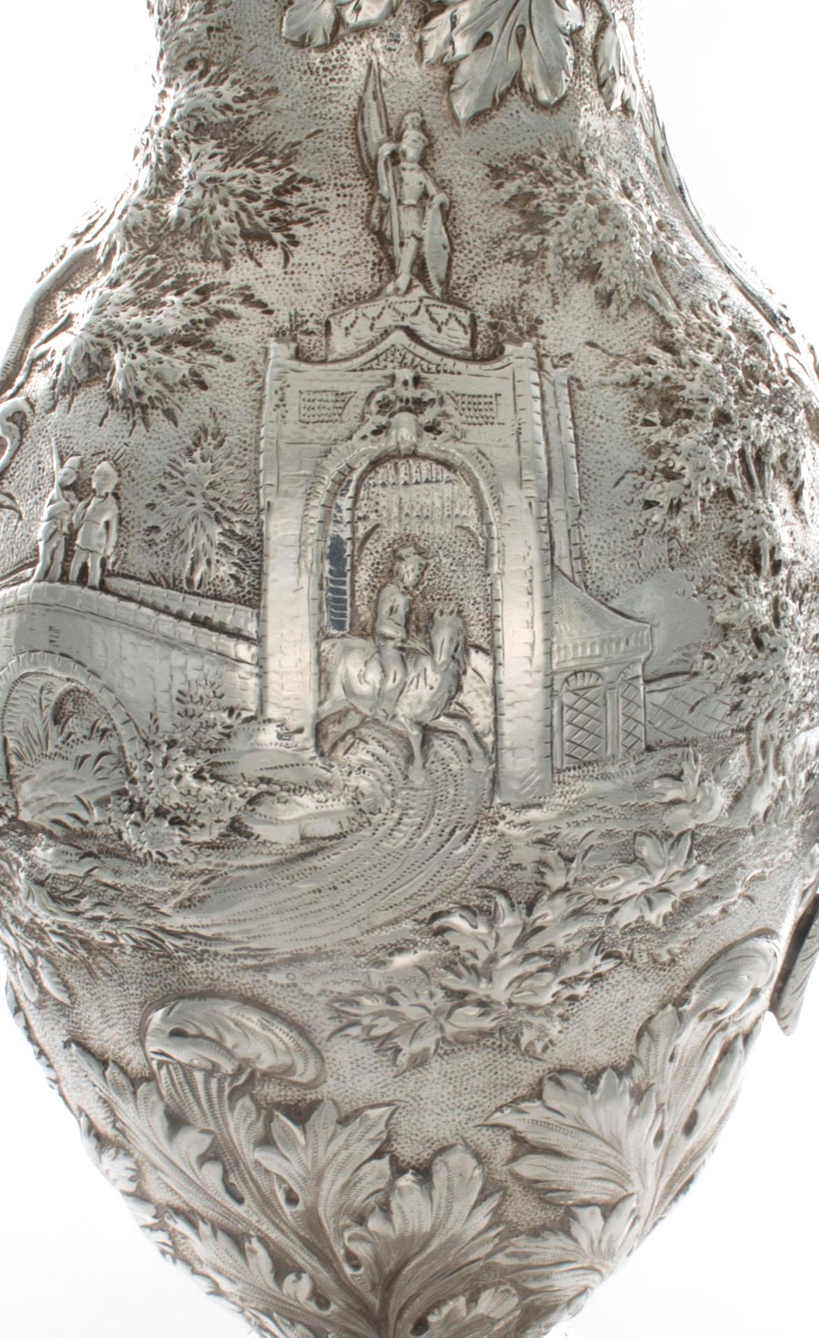 This outstanding S. Kirk & Son Ewer features scenes of a man on horseback leaving home going across a bridge, through the gatehouse, and across the water that features ducks in the water. The design surrounds the entire ewer. There is well executed