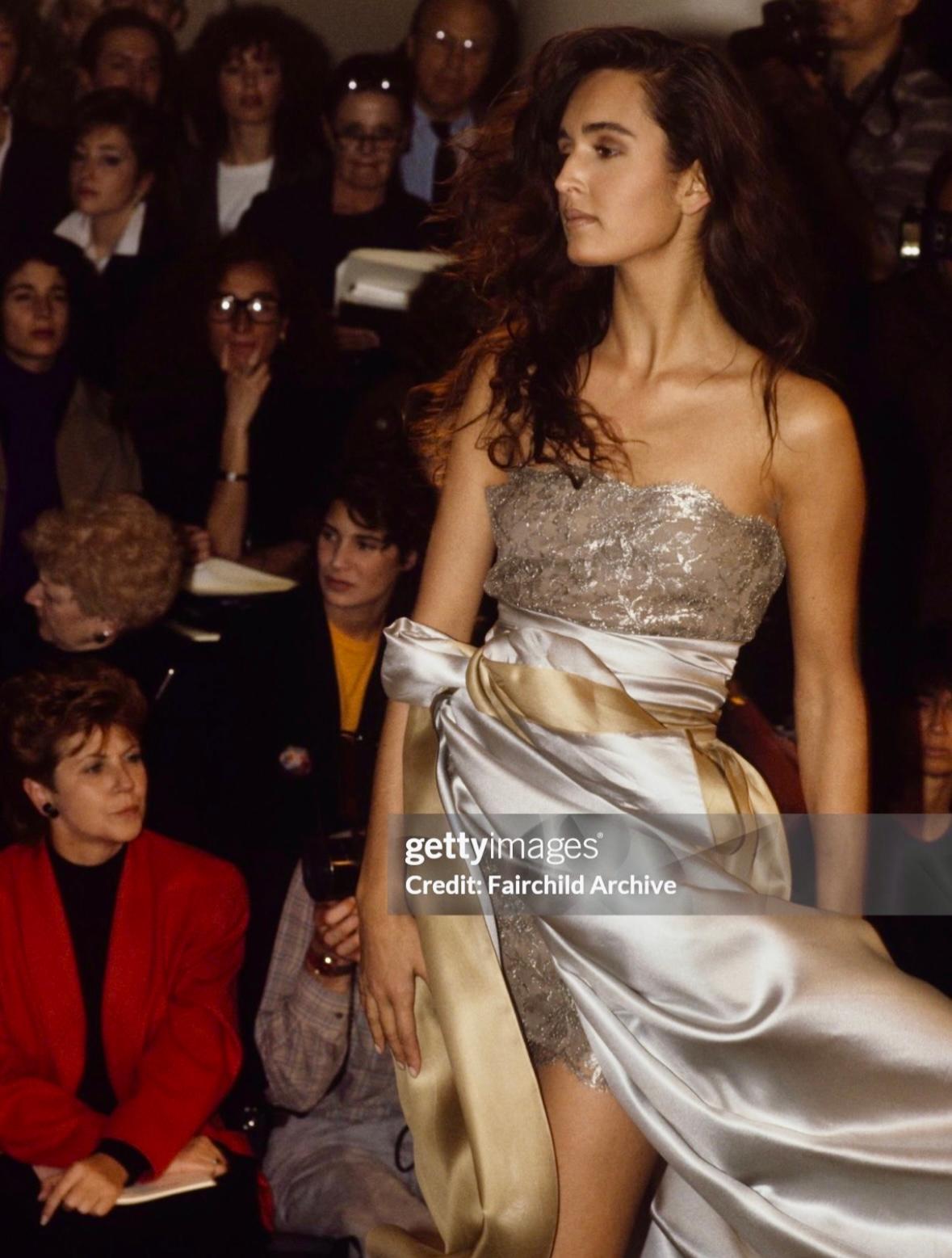 Este vestido de cóctel de la pasarela Calvin Klein Primavera/Verano 1988 está confeccionado en encaje floral plateado metalizado. El diseño sin tirantes presenta una silueta entallada con bordes festoneados que añaden un toque delicado. Gail Elliott