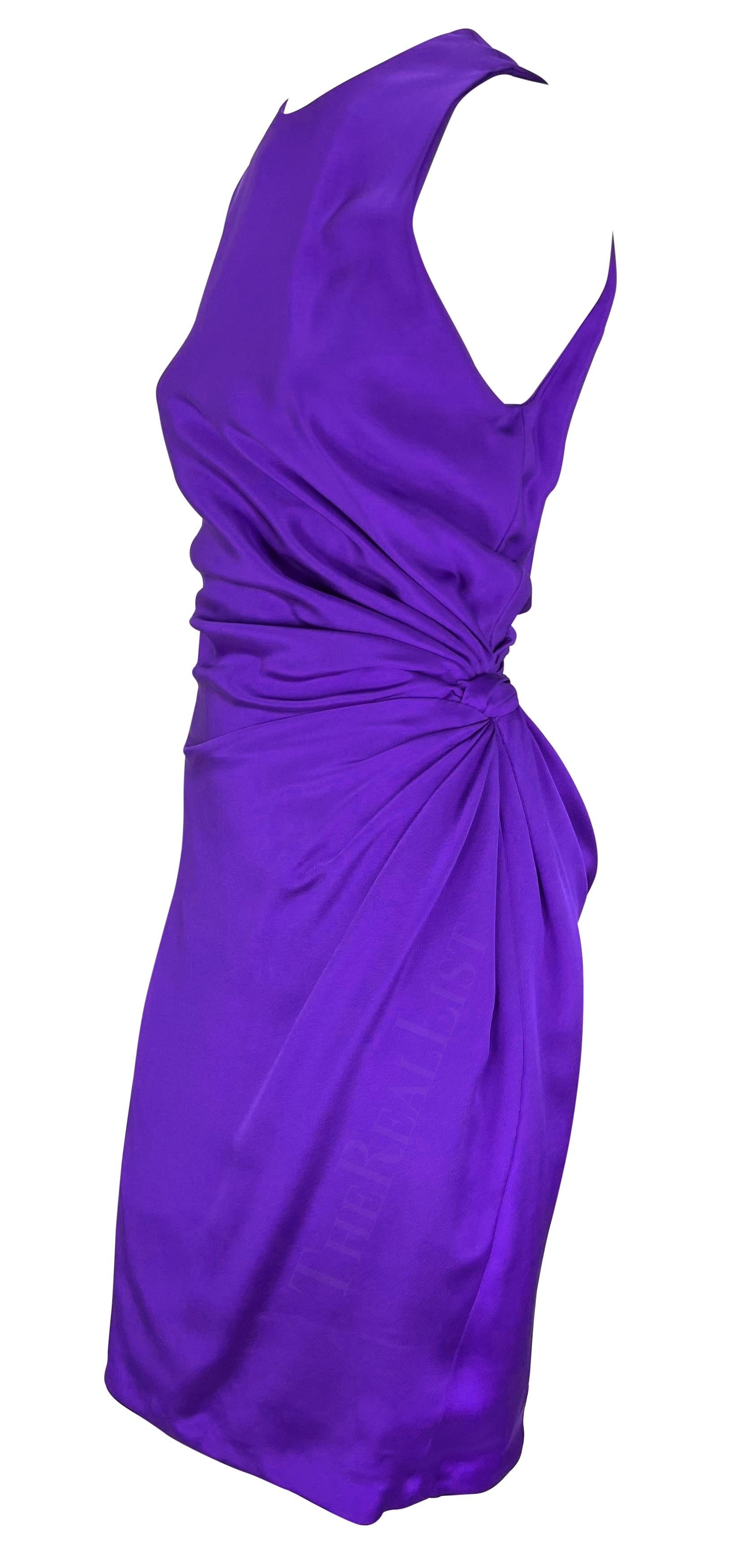Présentation d'une robe midi Gianni Versace d'un violet éclatant, conçue par Gianni Versace. Issue de la collection printemps/été 1991, cette robe présente une encolure ras du cou et des fermetures à boutons sur une épaule. La robe est complétée par