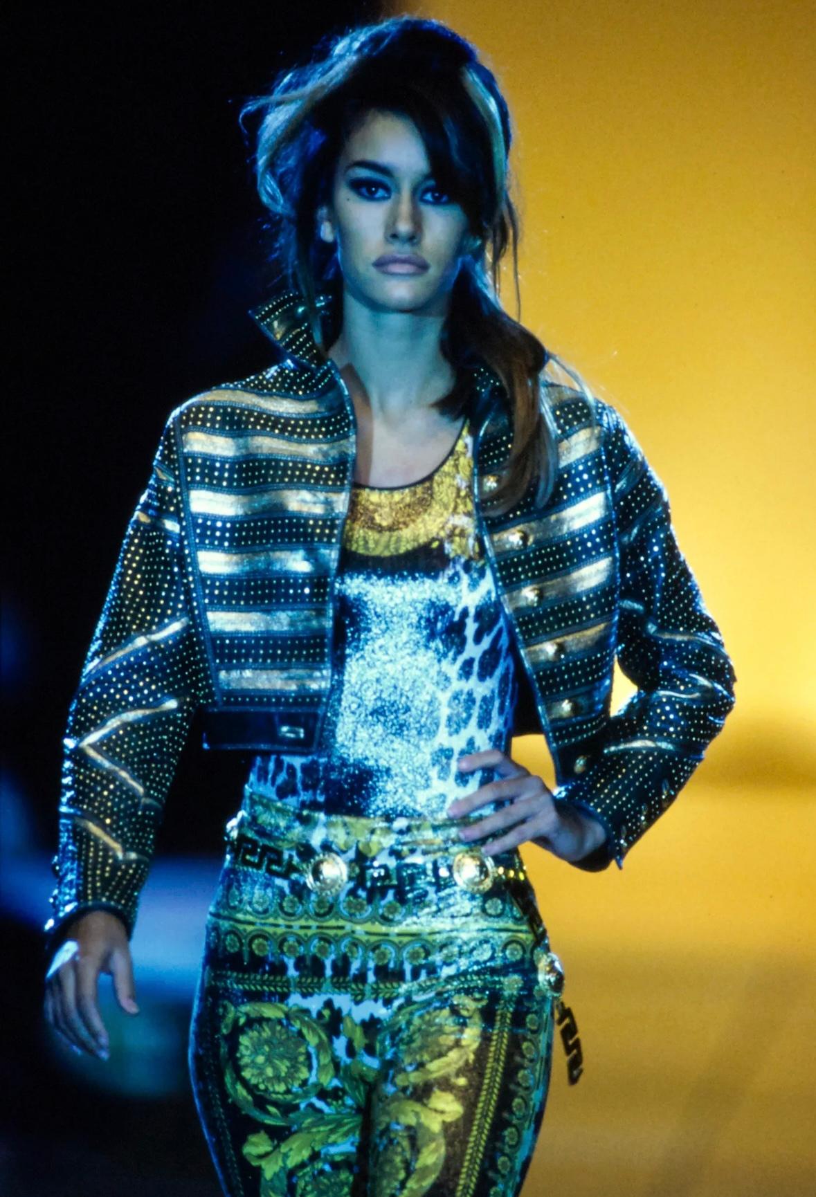 Esta chaqueta Gianni Versace de la colección Primavera 1992, parte del look de pasarela 58, modelada por Susan Holmes, está confeccionada en piel azul marino y presenta atrevidas franjas de piel metalizada dorada adornadas con tachuelas doradas. La