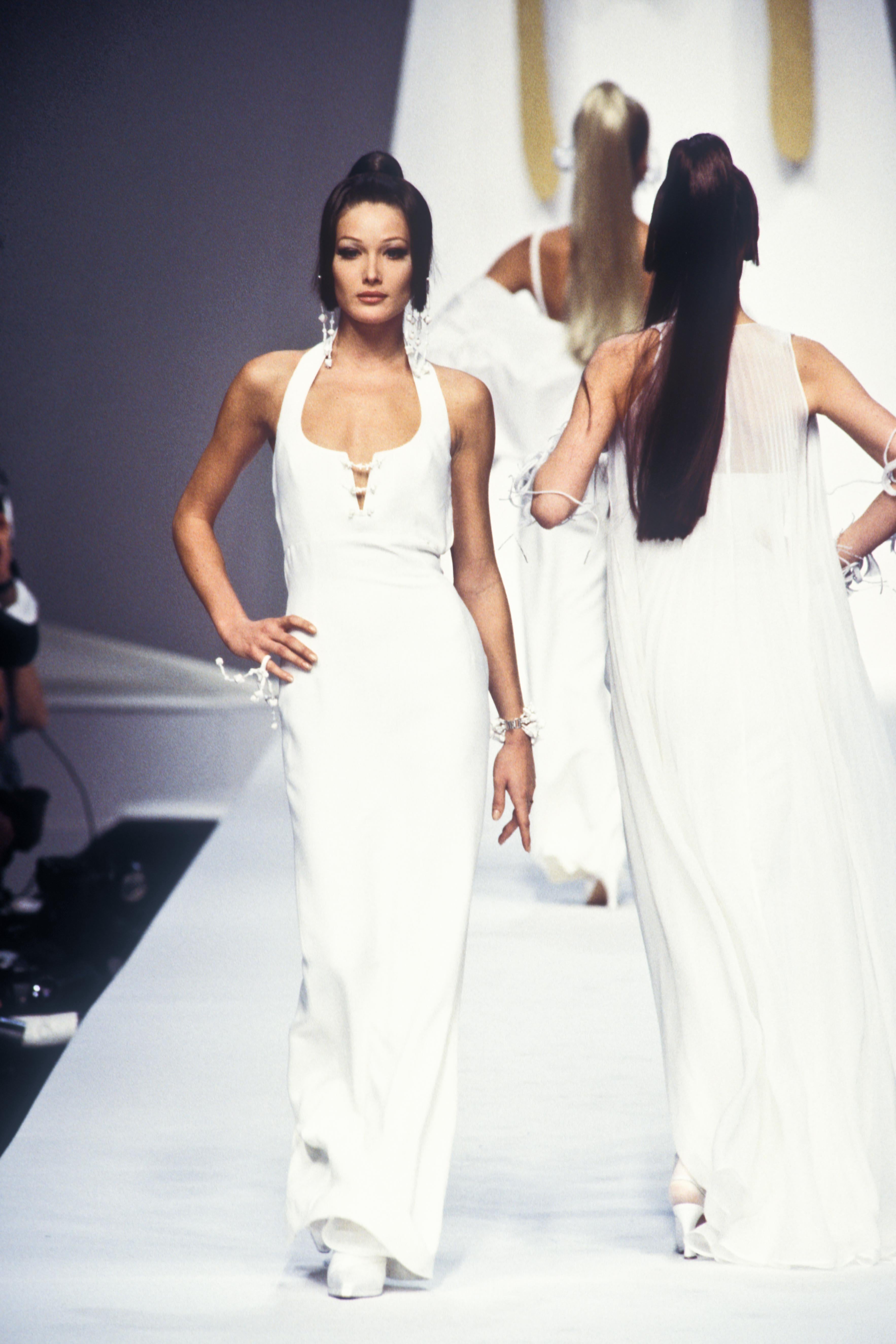 Dieses atemberaubende schwarze Kleid mit Neckholder-Ausschnitt aus der Frühjahr/Sommer-Kollektion 1993 von Claude Montana zeichnet sich durch einen Rundhalsausschnitt mit kleinem Einschnitt aus, der mit weißen Perlen im Brustbereich akzentuiert ist.